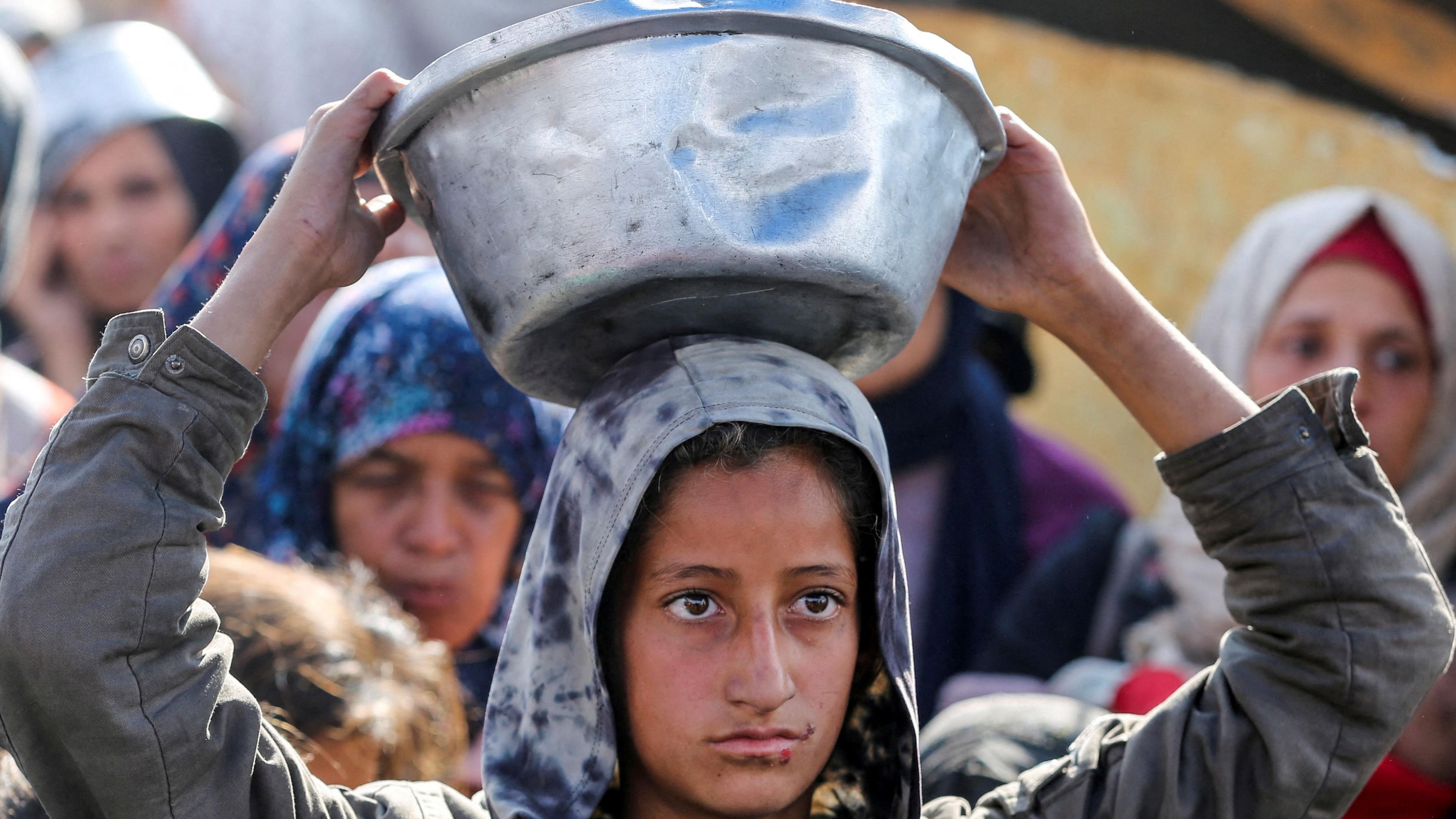 A Palestinian girl balances a tin bowl on her head as she collects cooked food from a charity kitchen