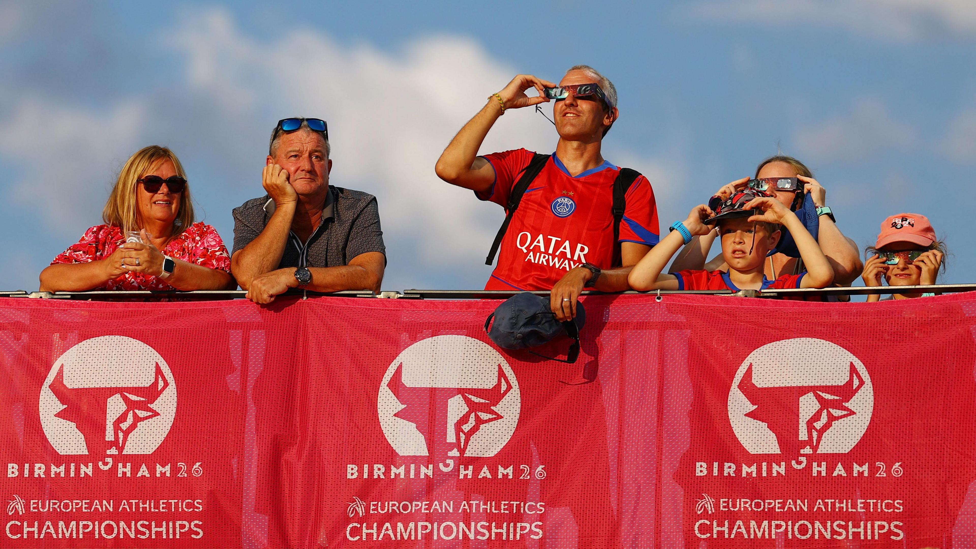 Spectators in the stands at the European Athletics Championships in Birmingham watch the solar eclipse through protective glasses during the evening session.