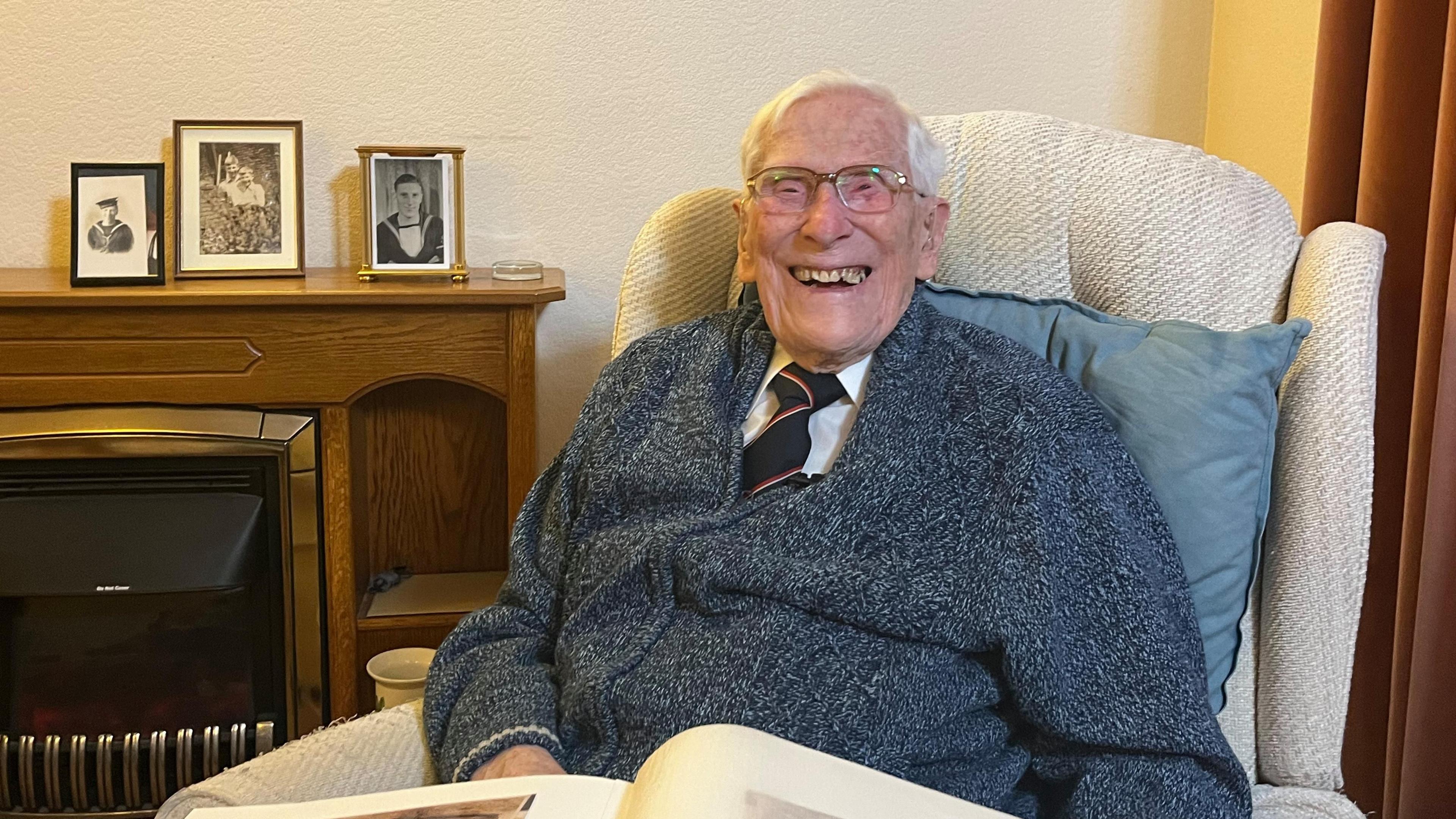 104-year-old John Daniels, laughing near framed photos of his Navy days