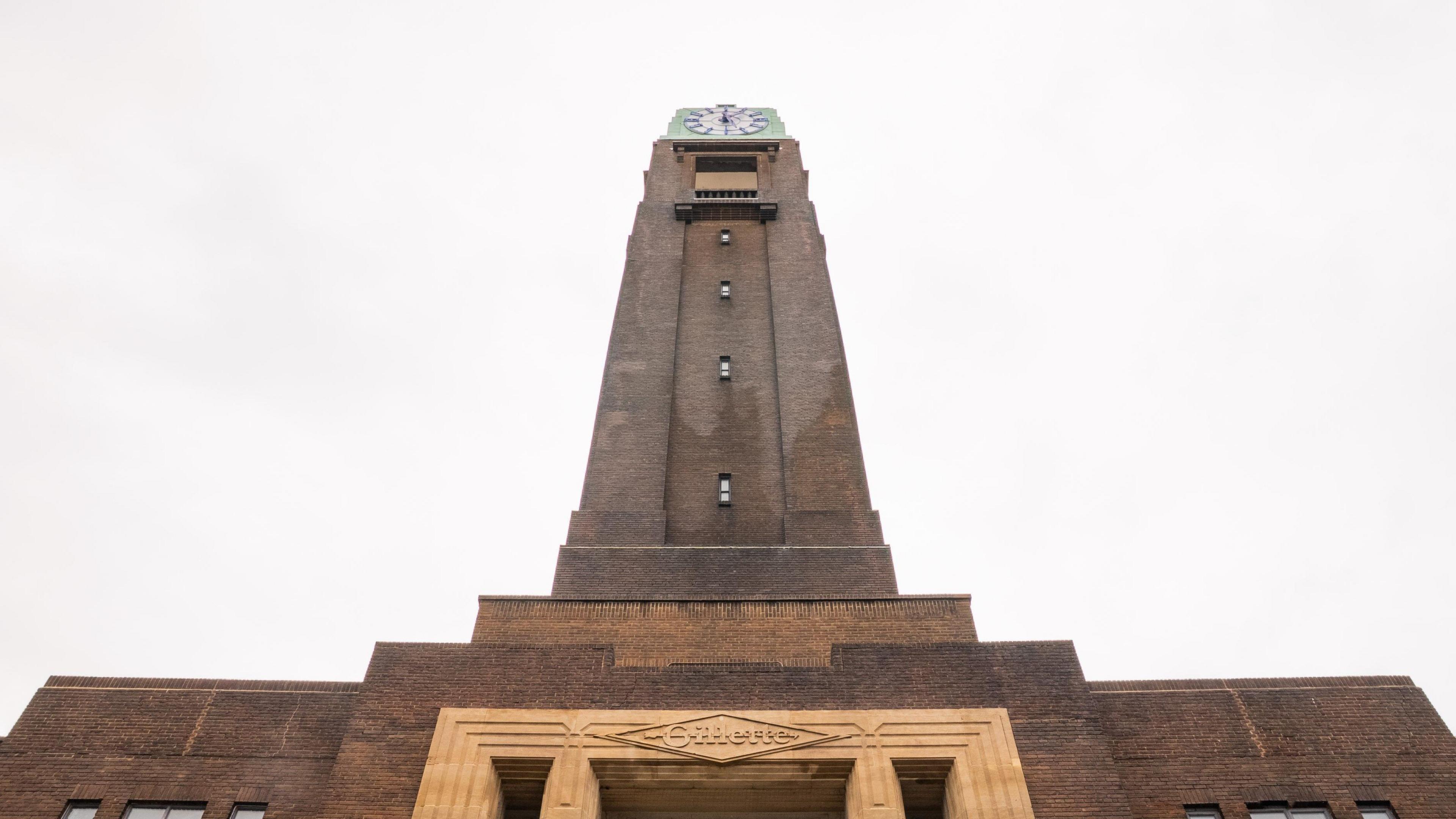 Looking up at the clock face from the ground, on top of a high brick tower.