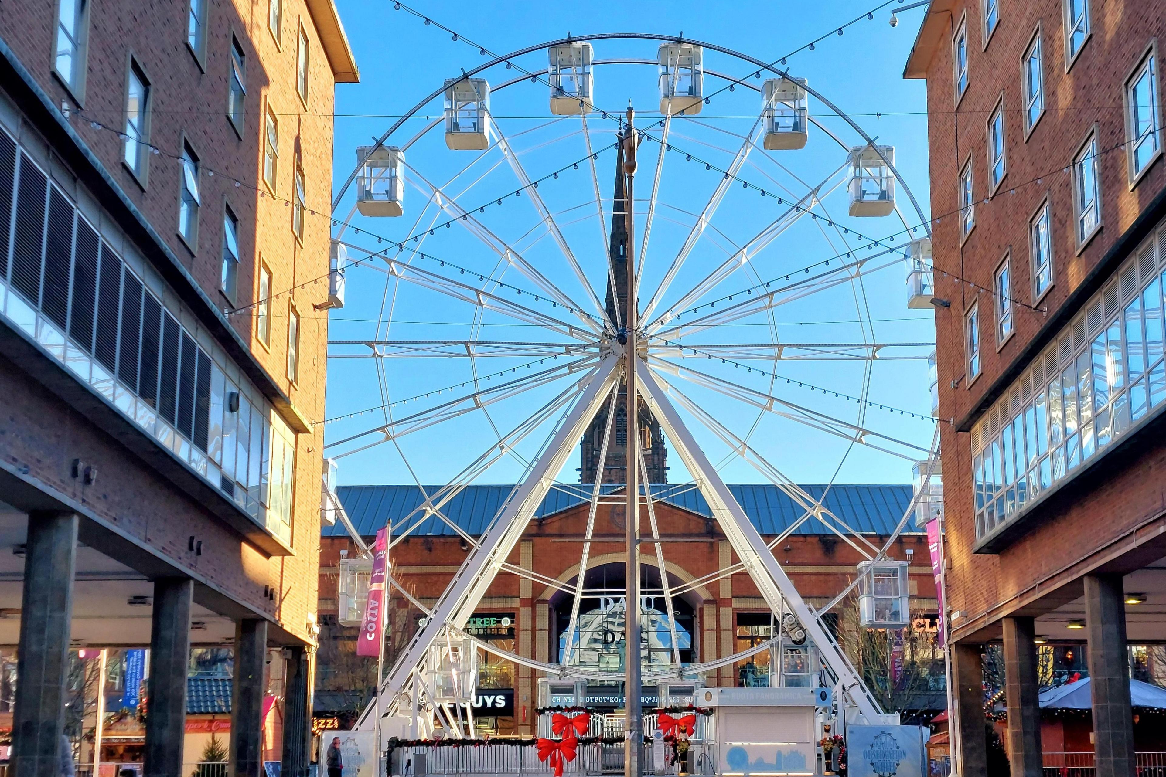 A big wheel is pictured in Coventry's Broadgate. Restaurants adorned with Christmas decorations can be seen behind with shops in the foreground.