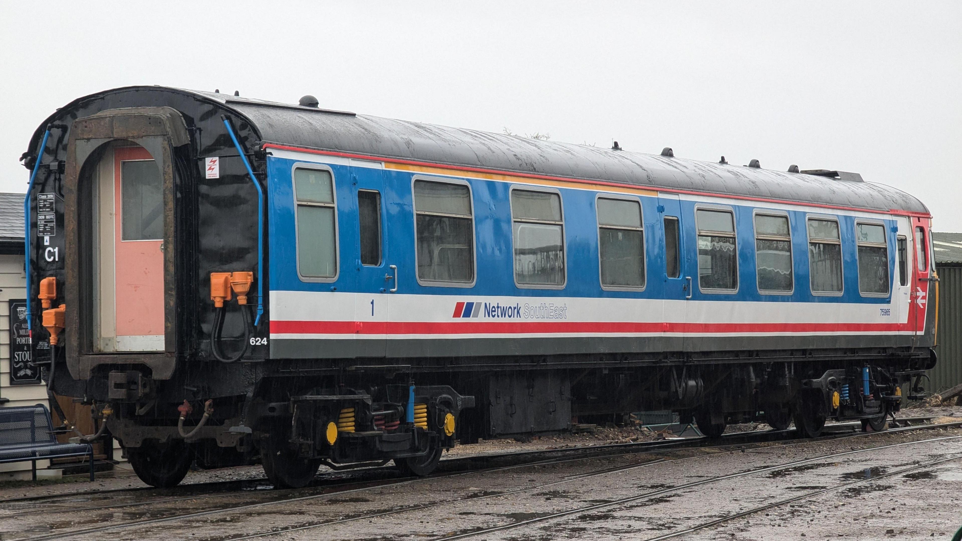 A view of the back and side of the Clacton Express. The rear of the train has been painted black with a red door. The side is largely blue with some white and red details.