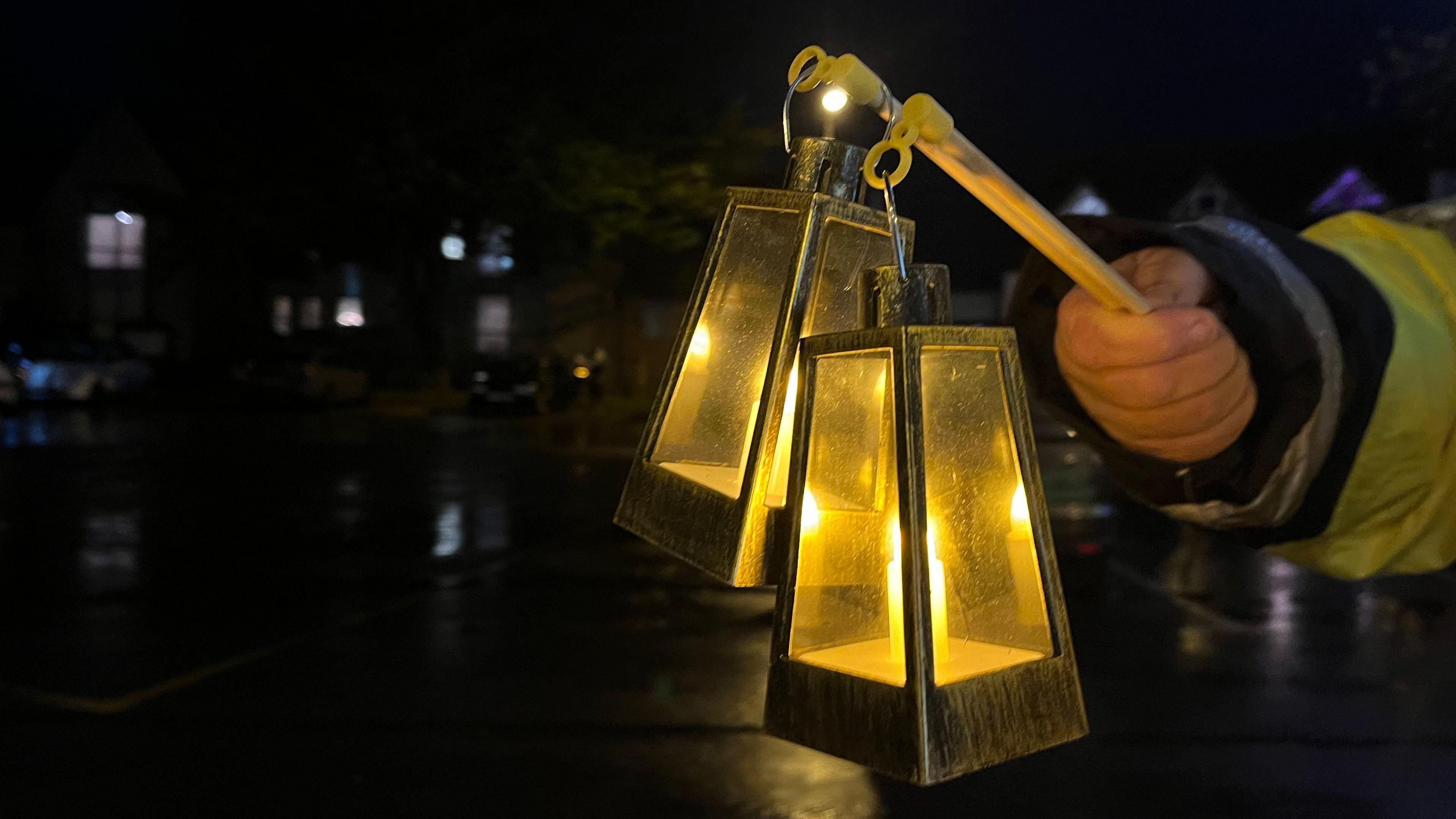 An arm holding two metal lanterns in a dark town