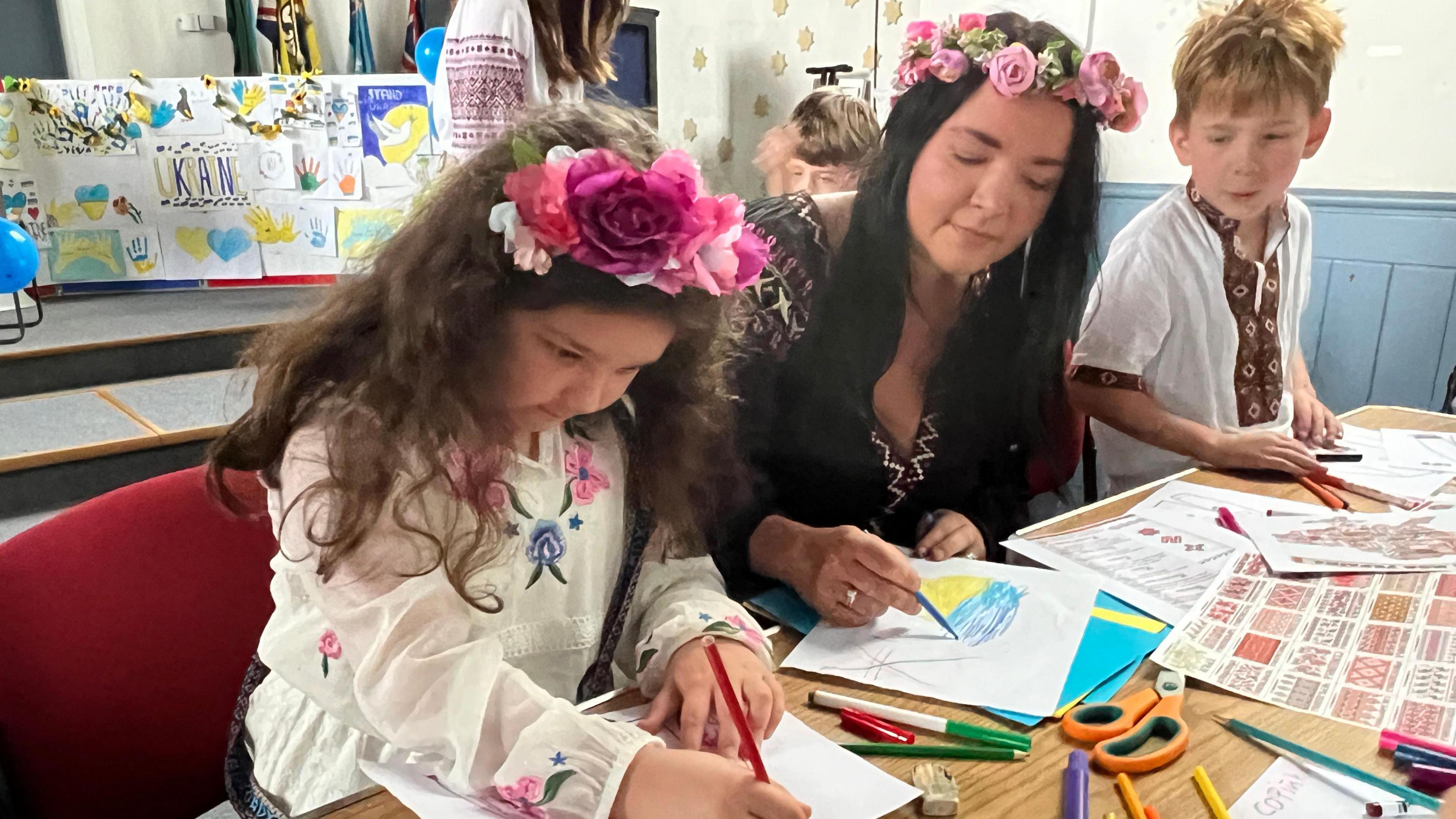 Both Leia and Natalie wear floral headbands while drawing at a table