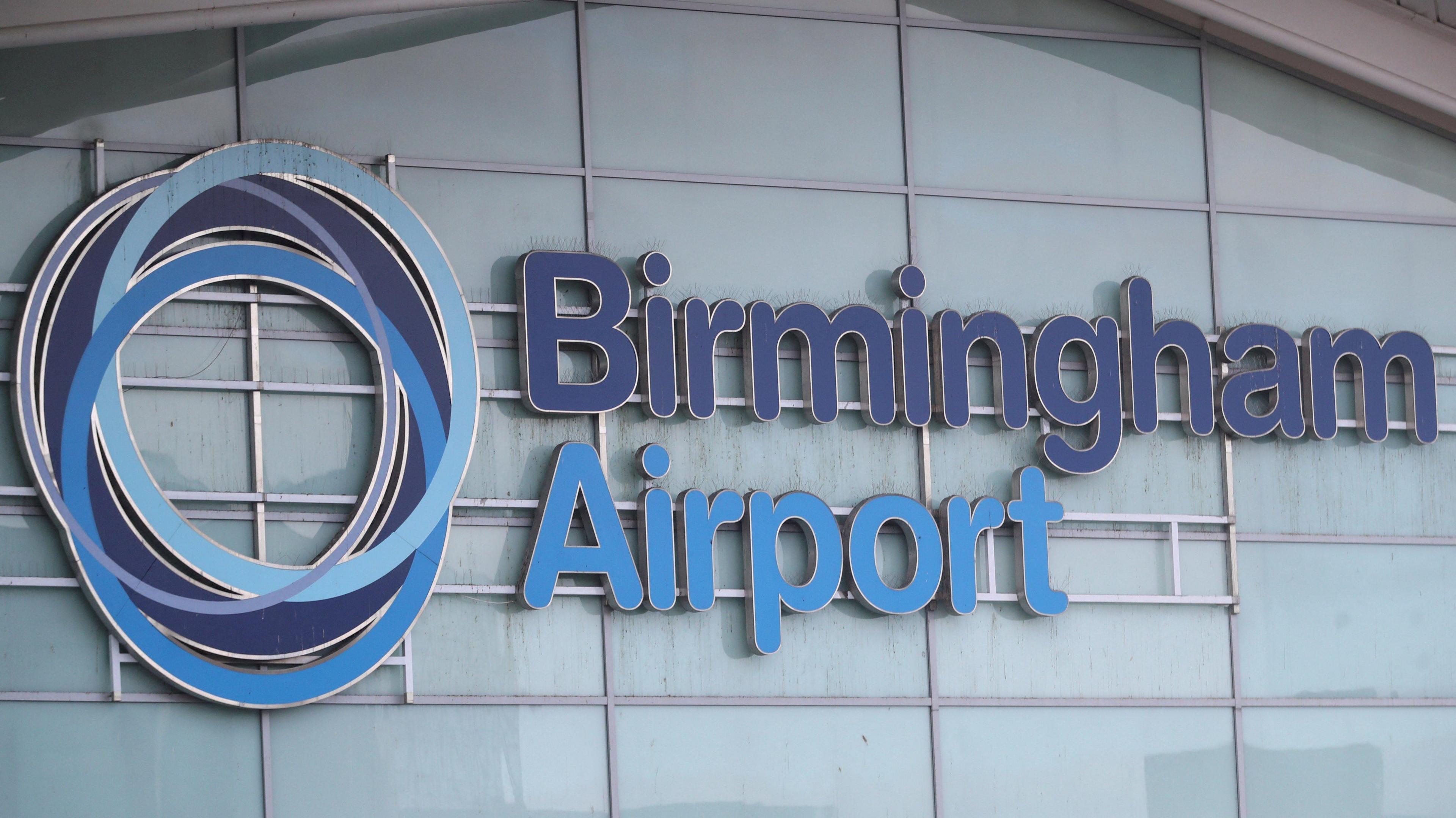 The Birmingham Airport sign on the side of a building with Birmingham in dark blue letters and airport in light blue letters. The airport's circular symbol is to the left of the words.