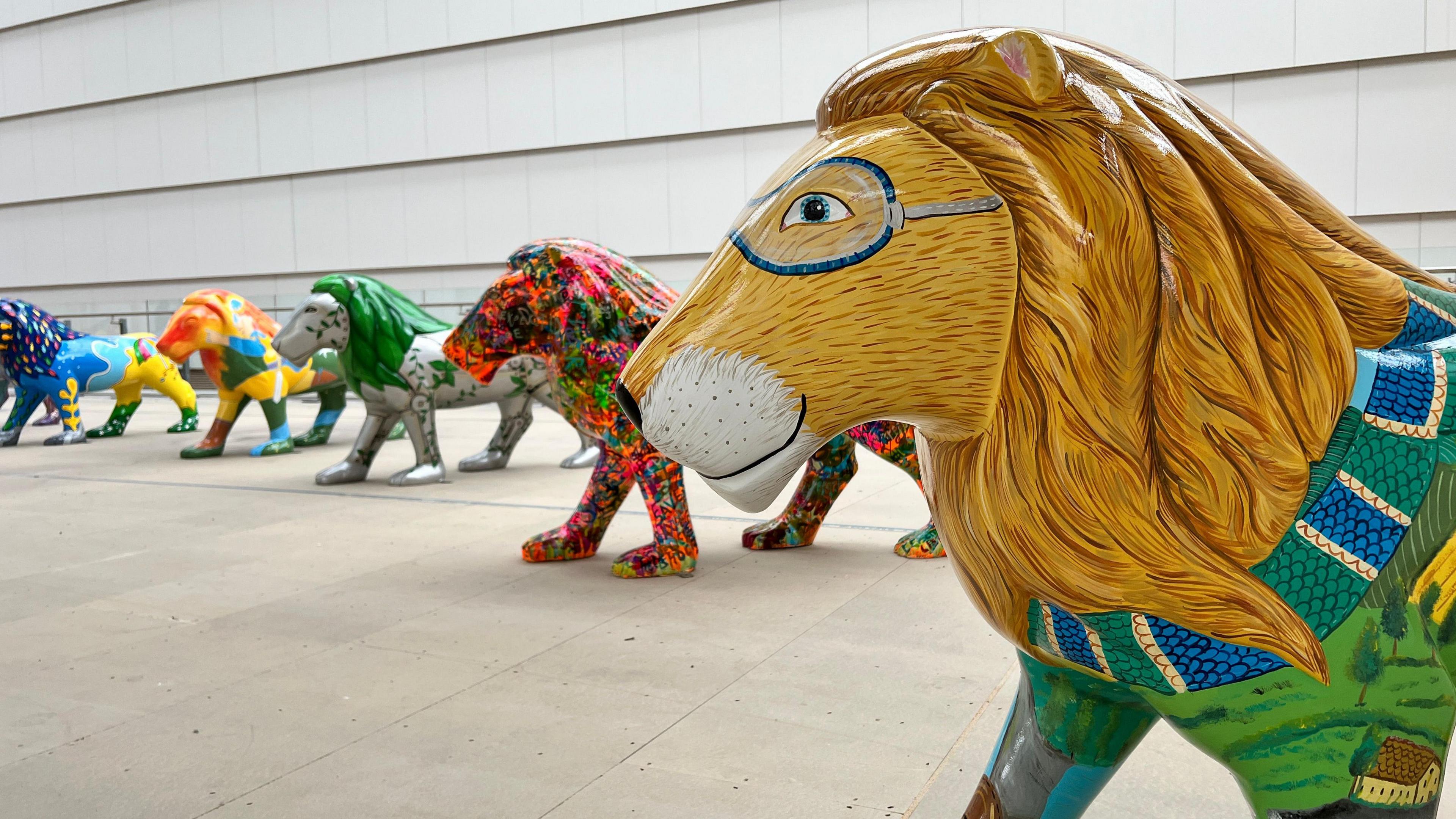 A line of lions arranged in a semi-circle, all of which are covered with very bright colourful designs.