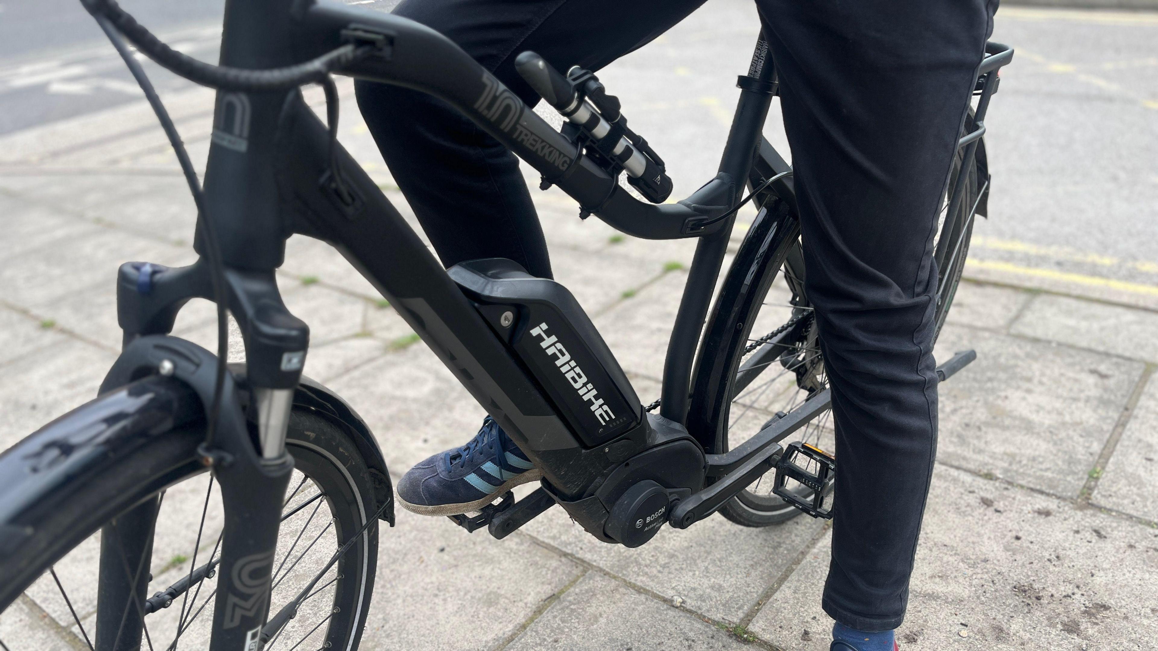 A picture of someone riding on an e-bike. They are wearing black trousers and blue striped shoes.