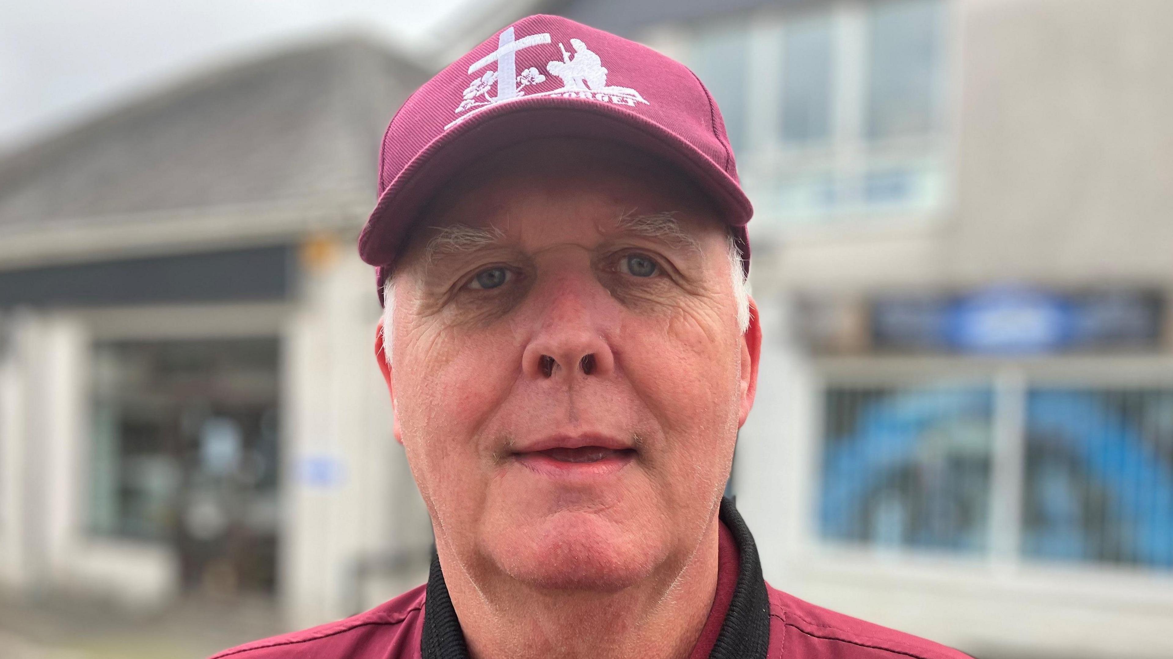 Man with baseball cap on in front of shop