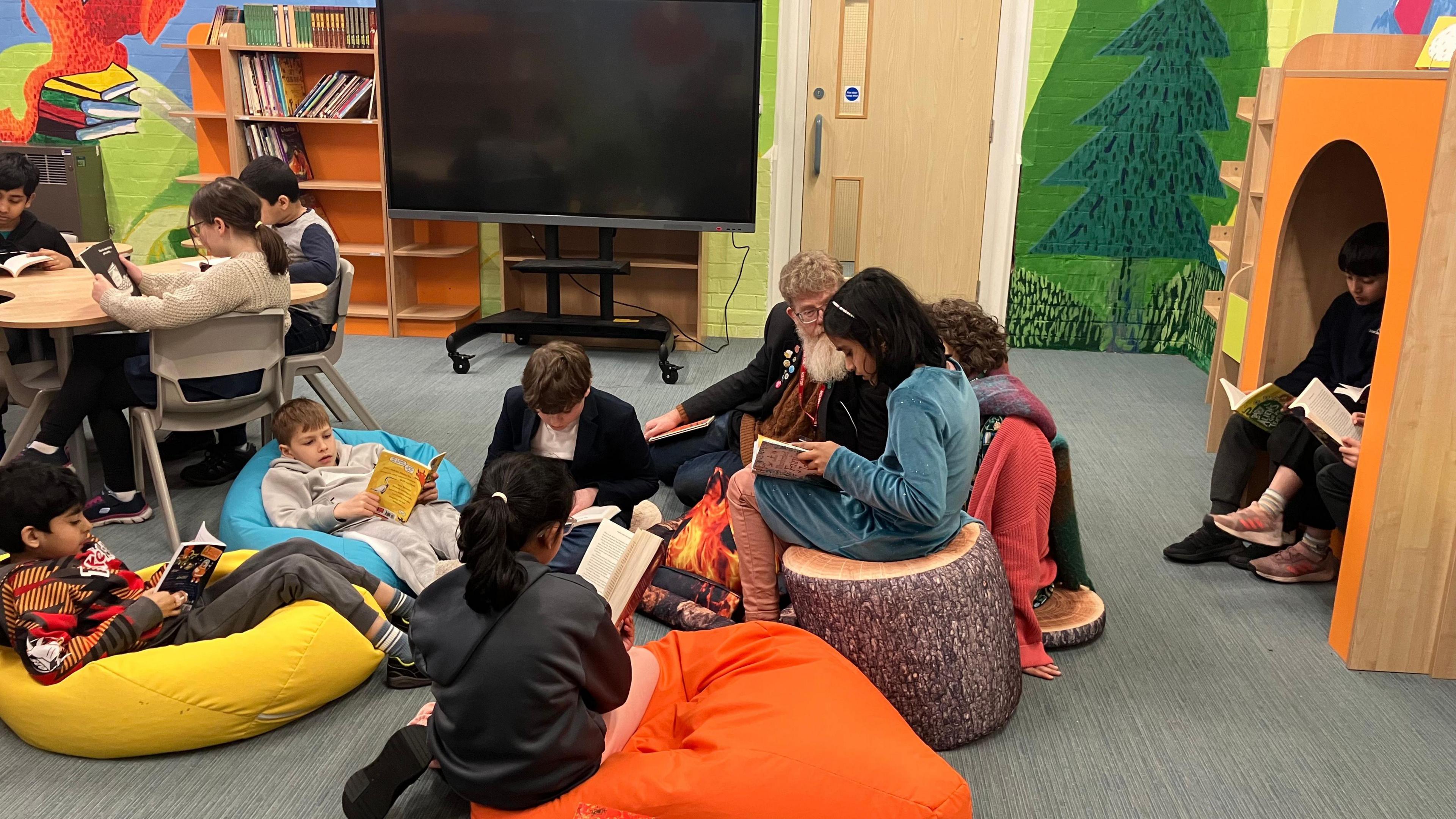 Children sat at tables and on beanbags and in a wooden cubby hole all reading after the library had been opened.