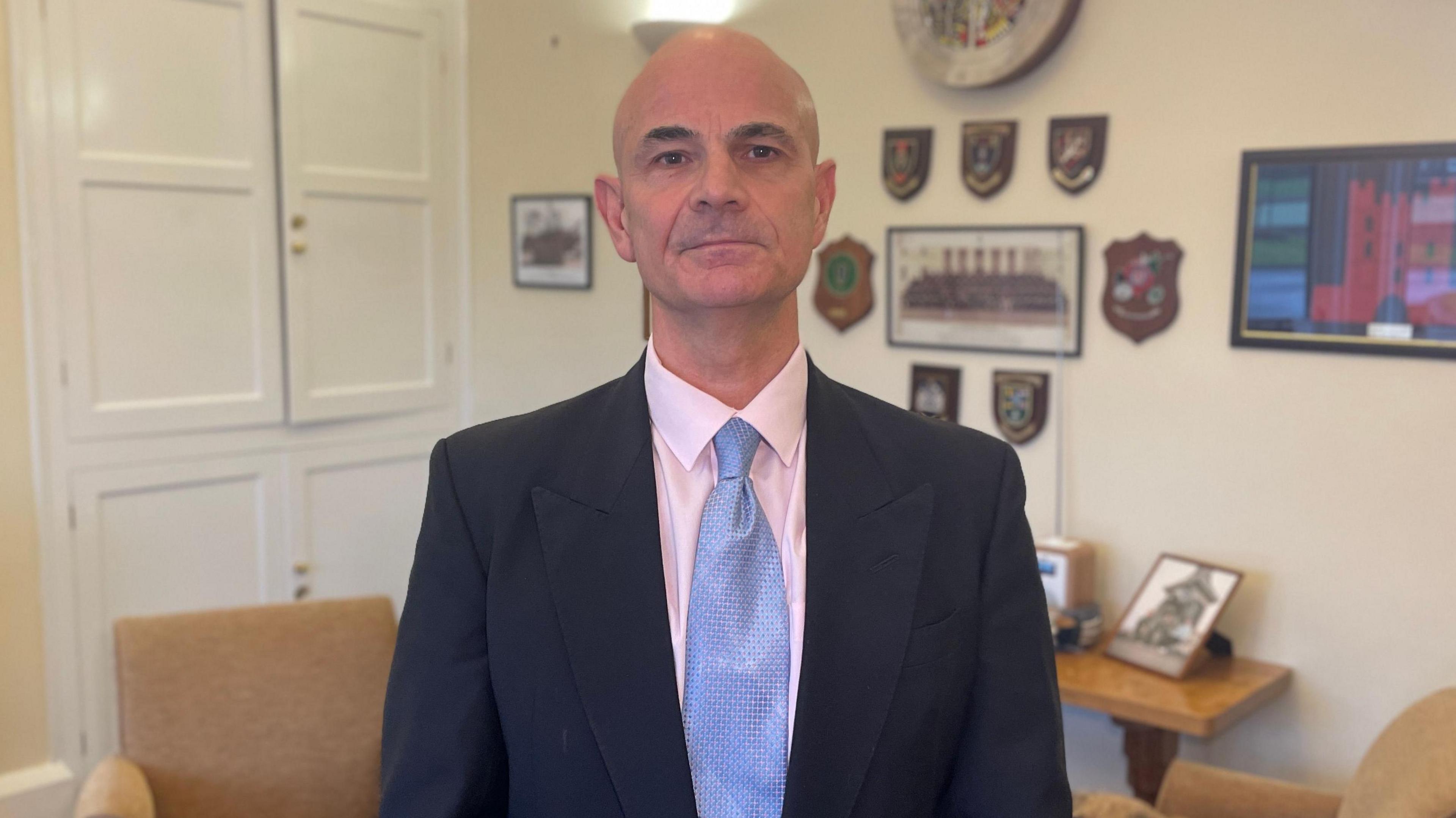 A man wearing a blue suit, pink shirt and blue tie looking directly towards the camera