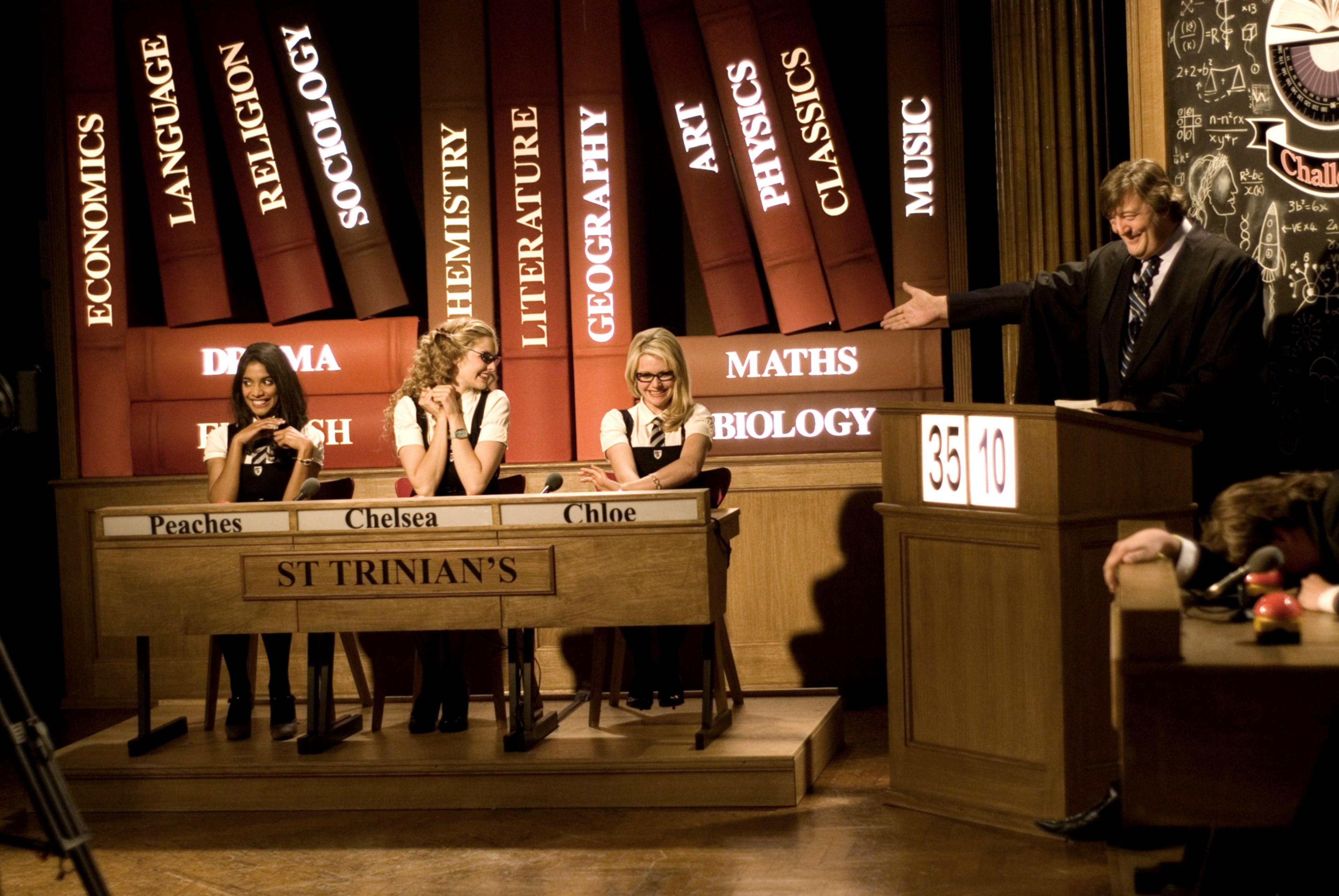 Amara Karan, Tamsin Egerton and Antonia Bernath sit behind desk in school quiz show, hosted by Sir Stephen Fry 