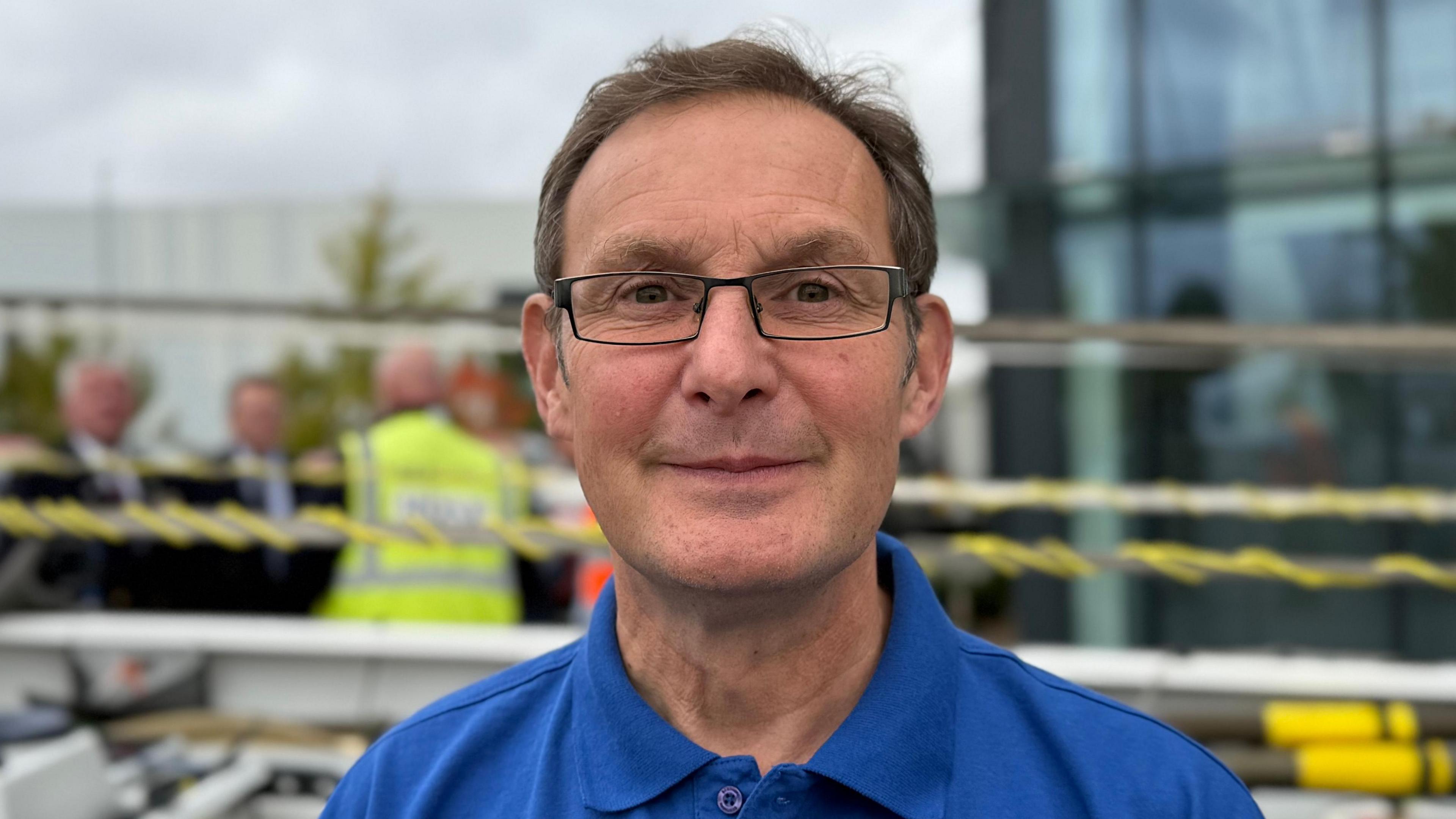 The head and shoulders of Andy Calame looking at the camera wearing a blue polo shirt. He is wearing rectangle framed glasses. He looks happy and is smiling at the camera.
