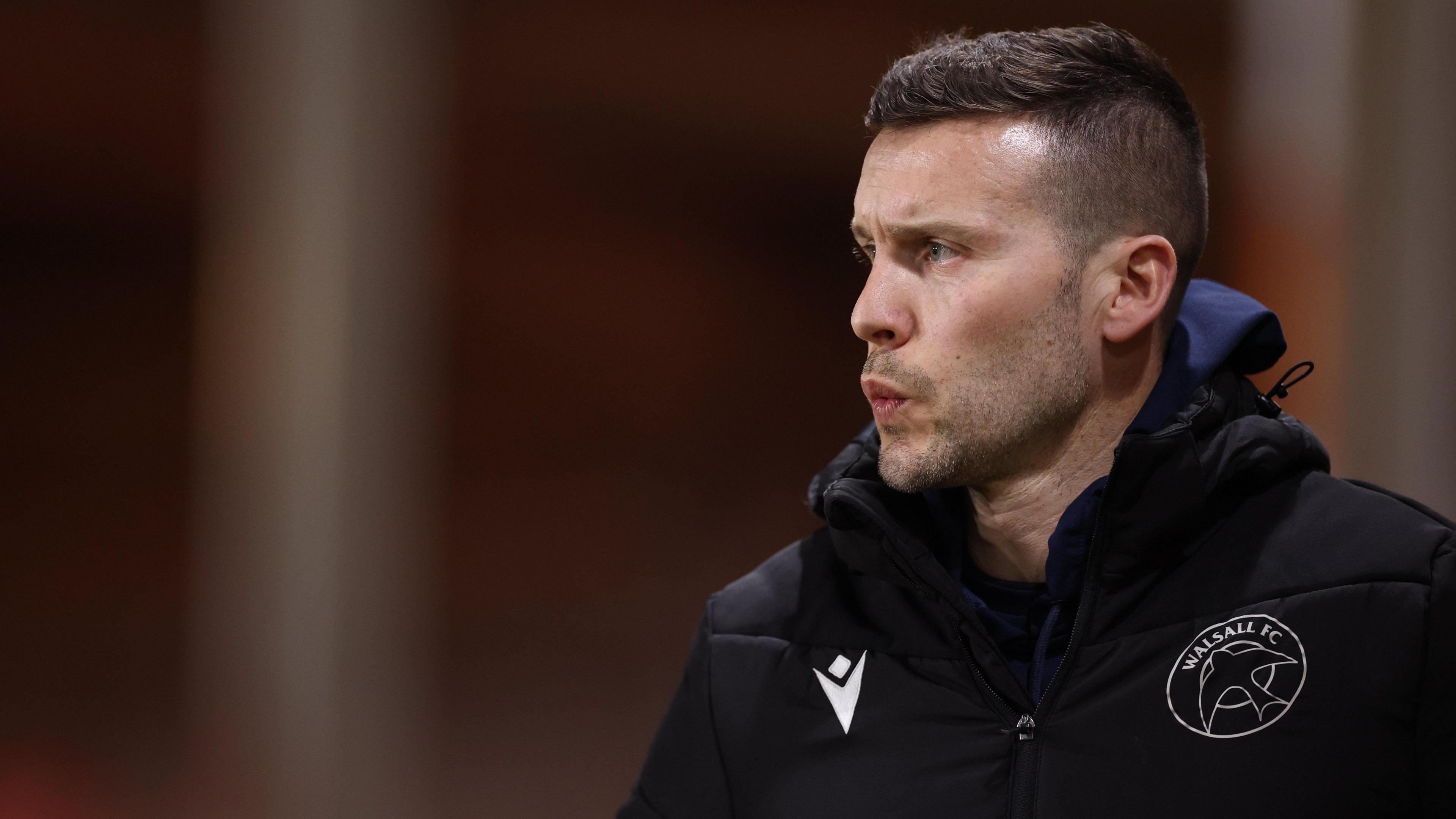 Mat Sadler watching on during Walsall's game against MK Dons while wearing a black puffer jacket