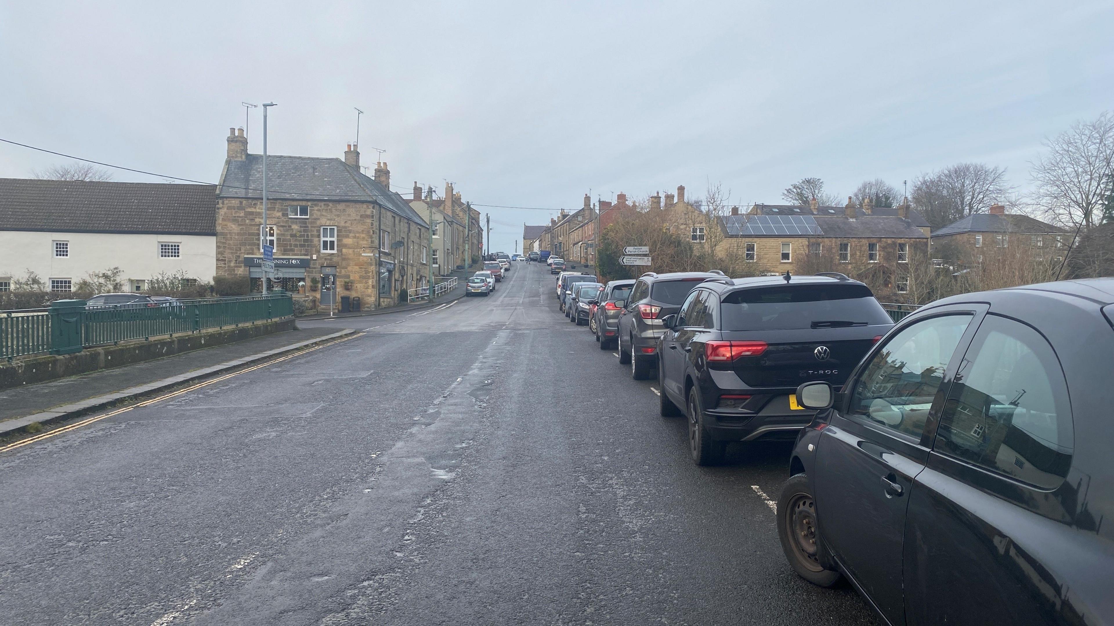 Felton high street stretches up a hill. The buildings are 18th Century, with cars parked on both sides.