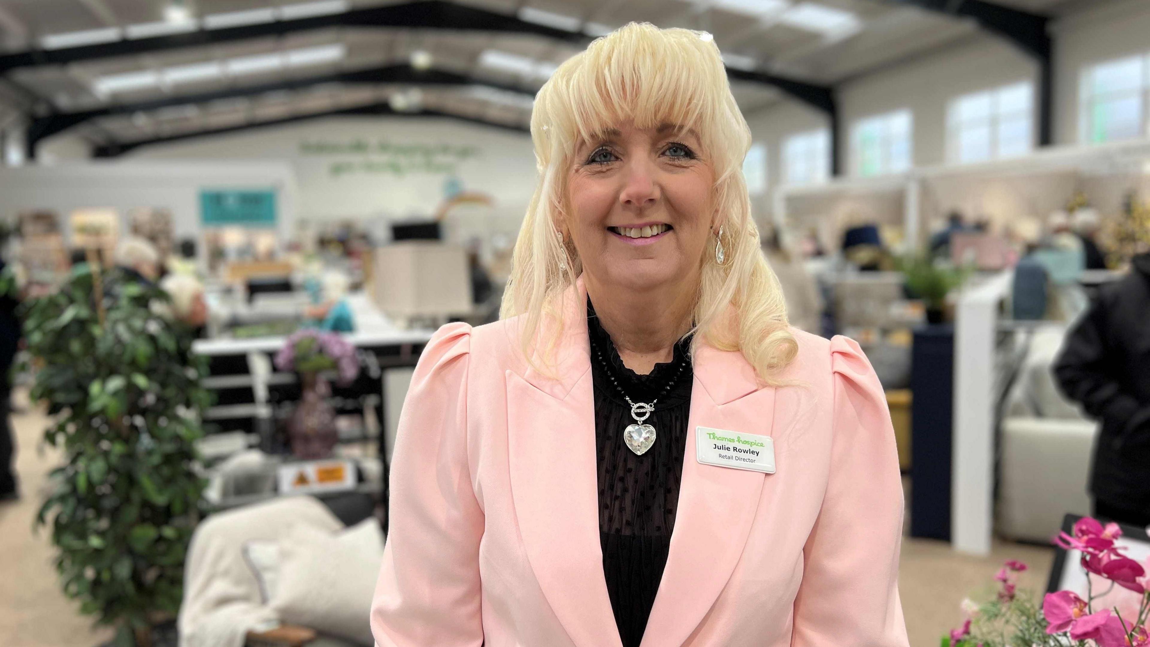 Julie Rowley, Director of retail at Thames Hospice smiling at the camera is wearing a black dress and pink short jacket.