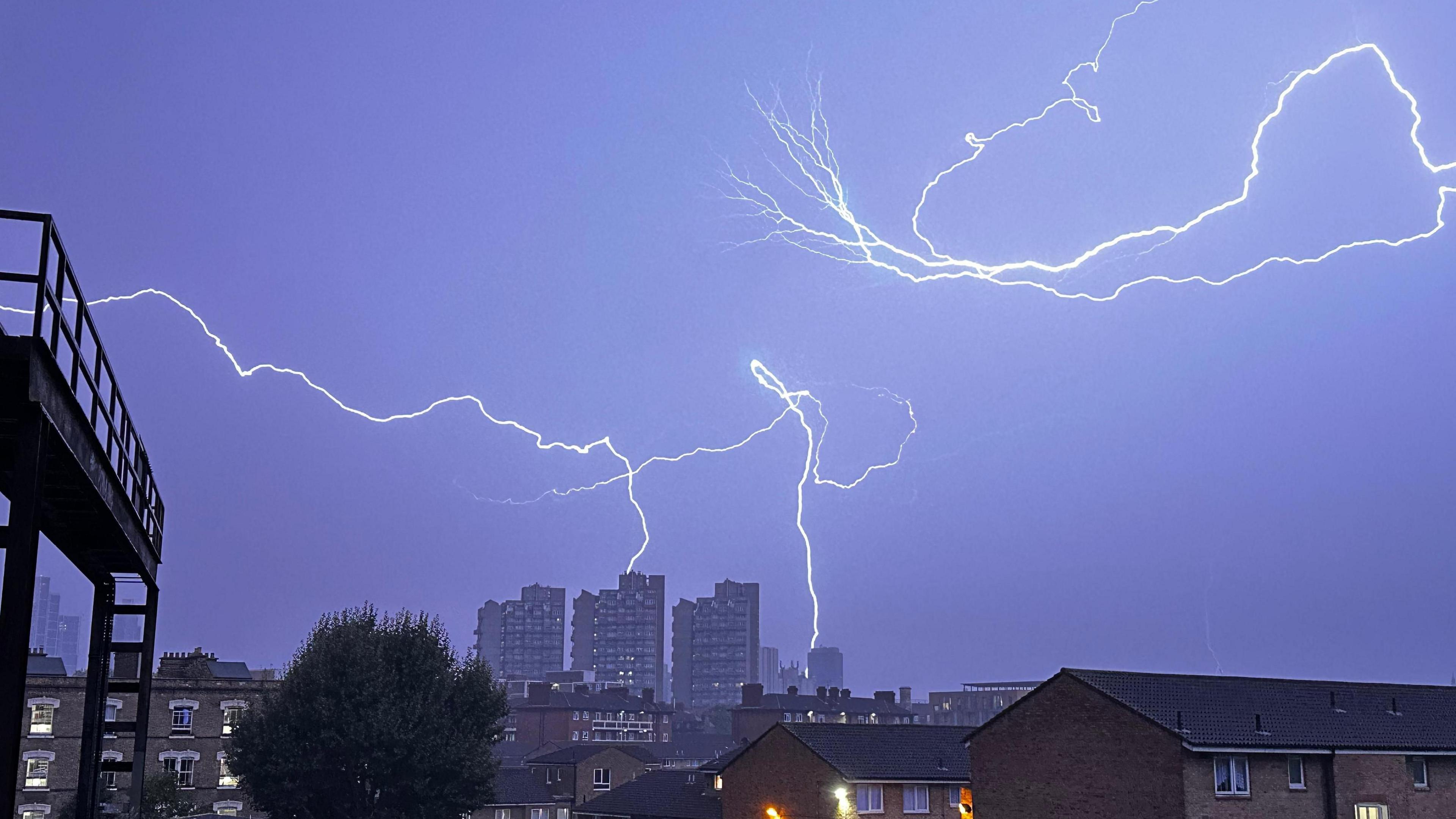 Fork lightning fills the darkened sky with some lightning hitting high rise buildings in the distance