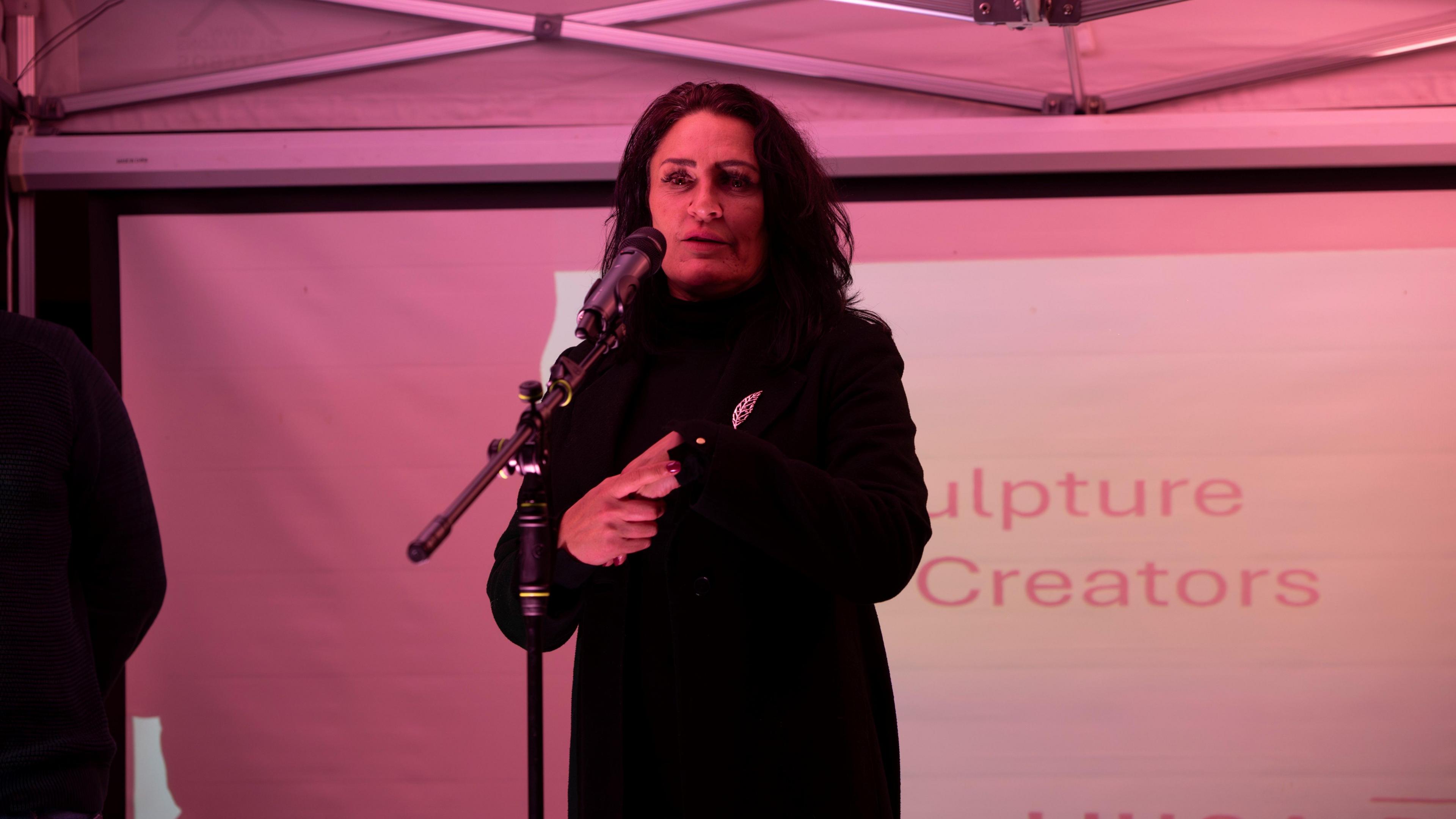 A woman with brown hair wearing all black talking on stage 