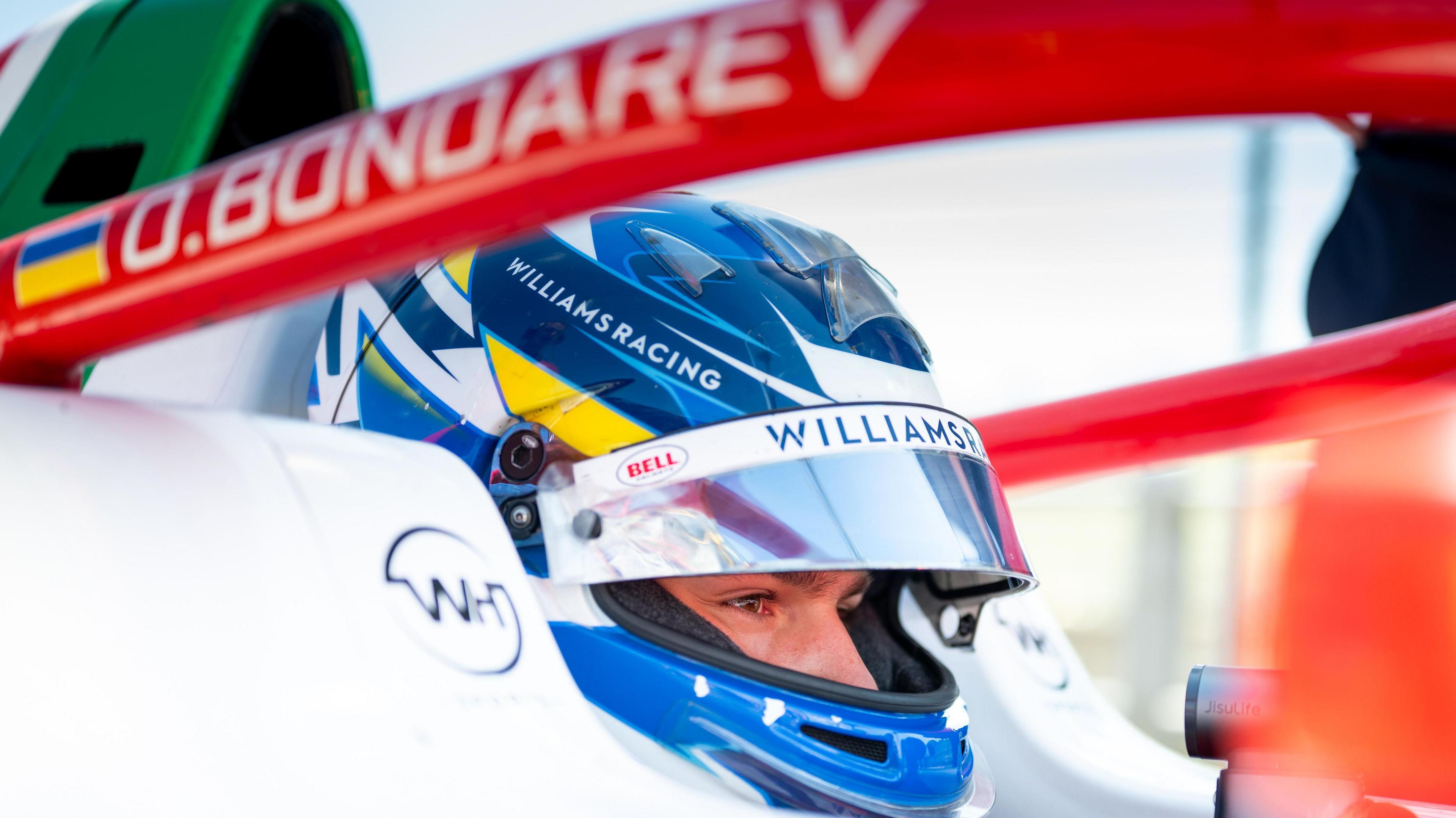 Bondarev in his racing car with his helmet on. His name is written on the car next to the Ukrainian flag.