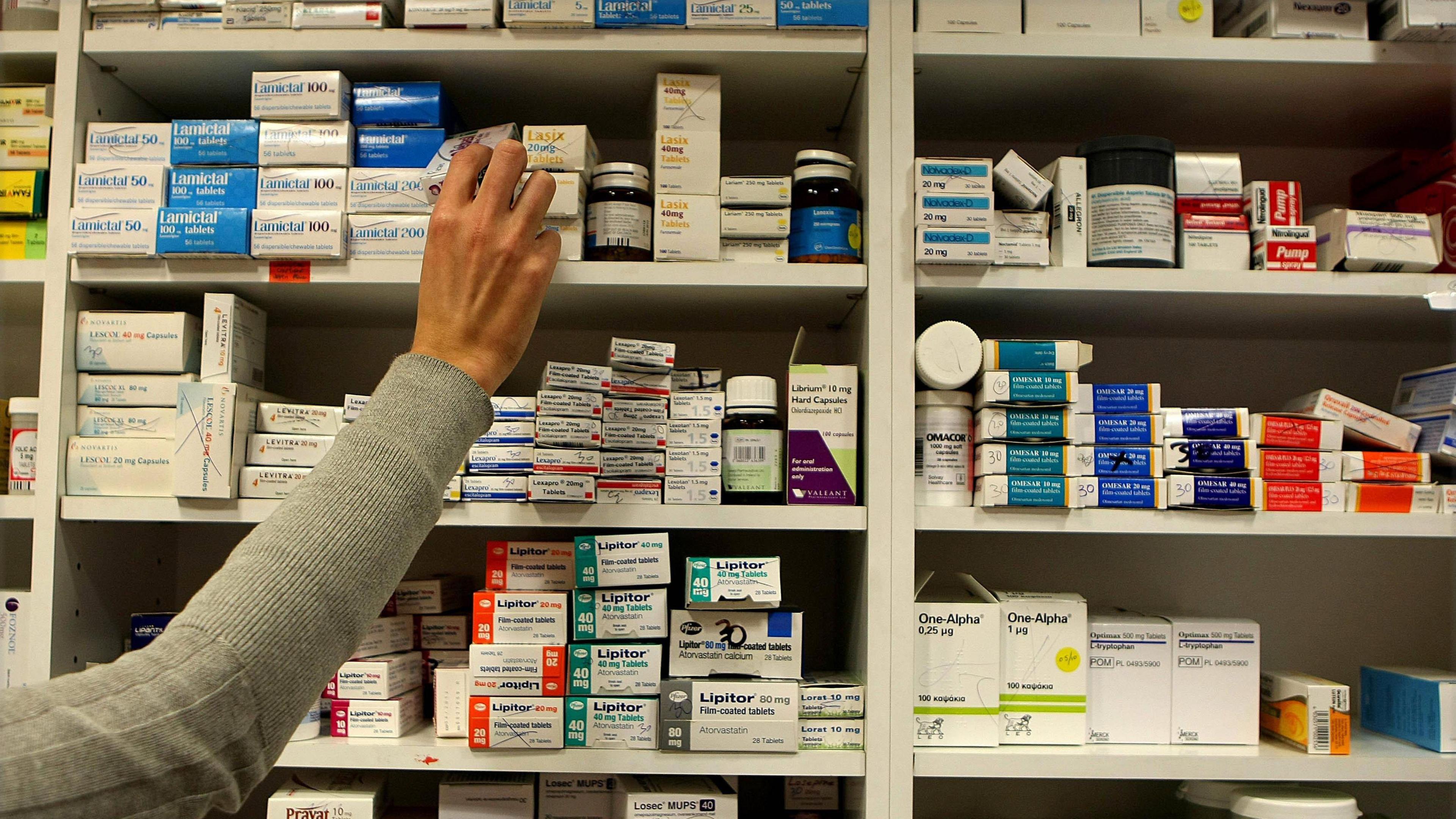 A picture of an arm reaching to an item within a pharmacy. The persons arm is covered with a grey sleeve.