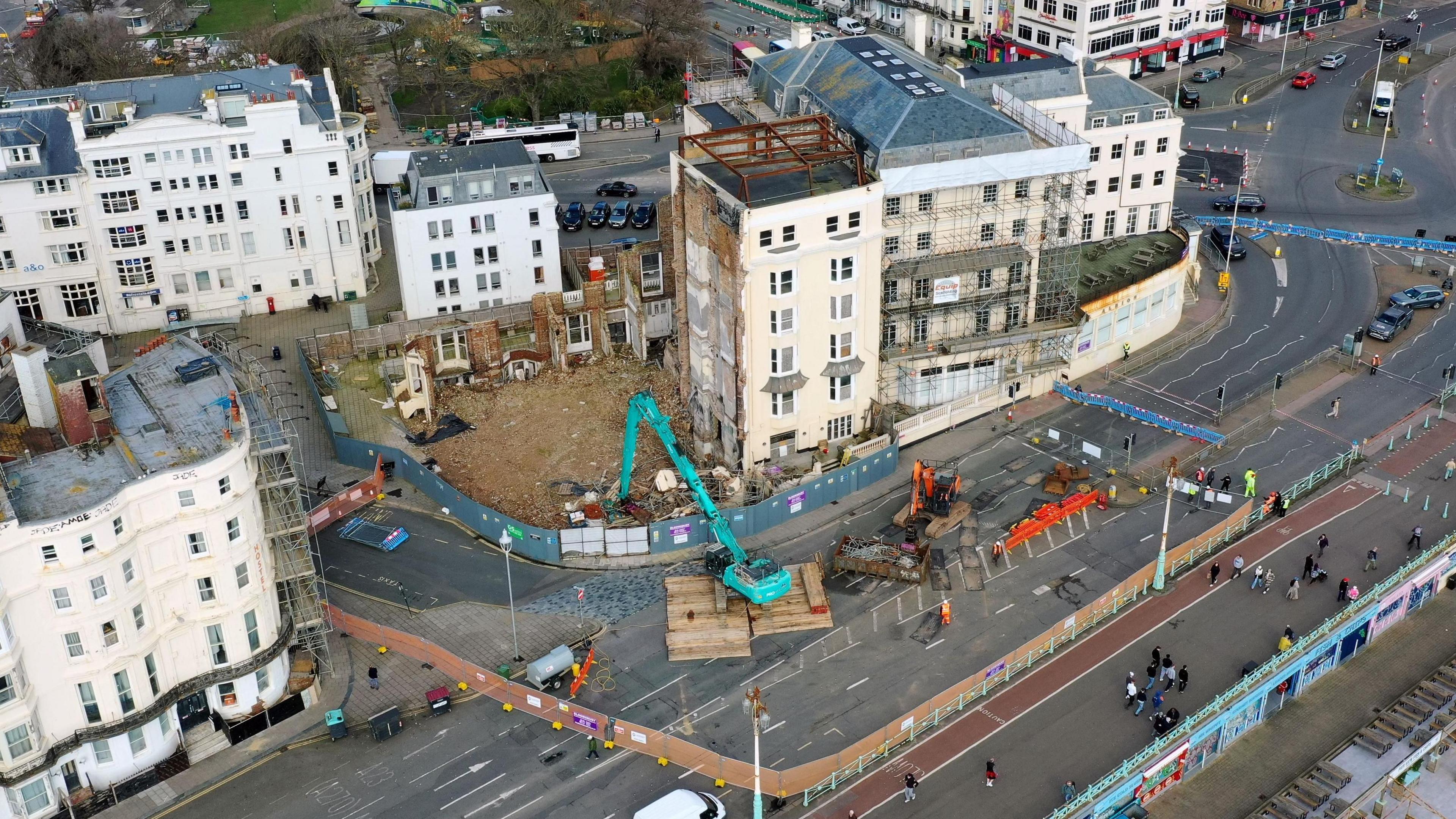 An aerial view of what is left of the Royal Albion Hotel on Brighton seafront. There is scaffolding around the cream building and three cranes on the road.