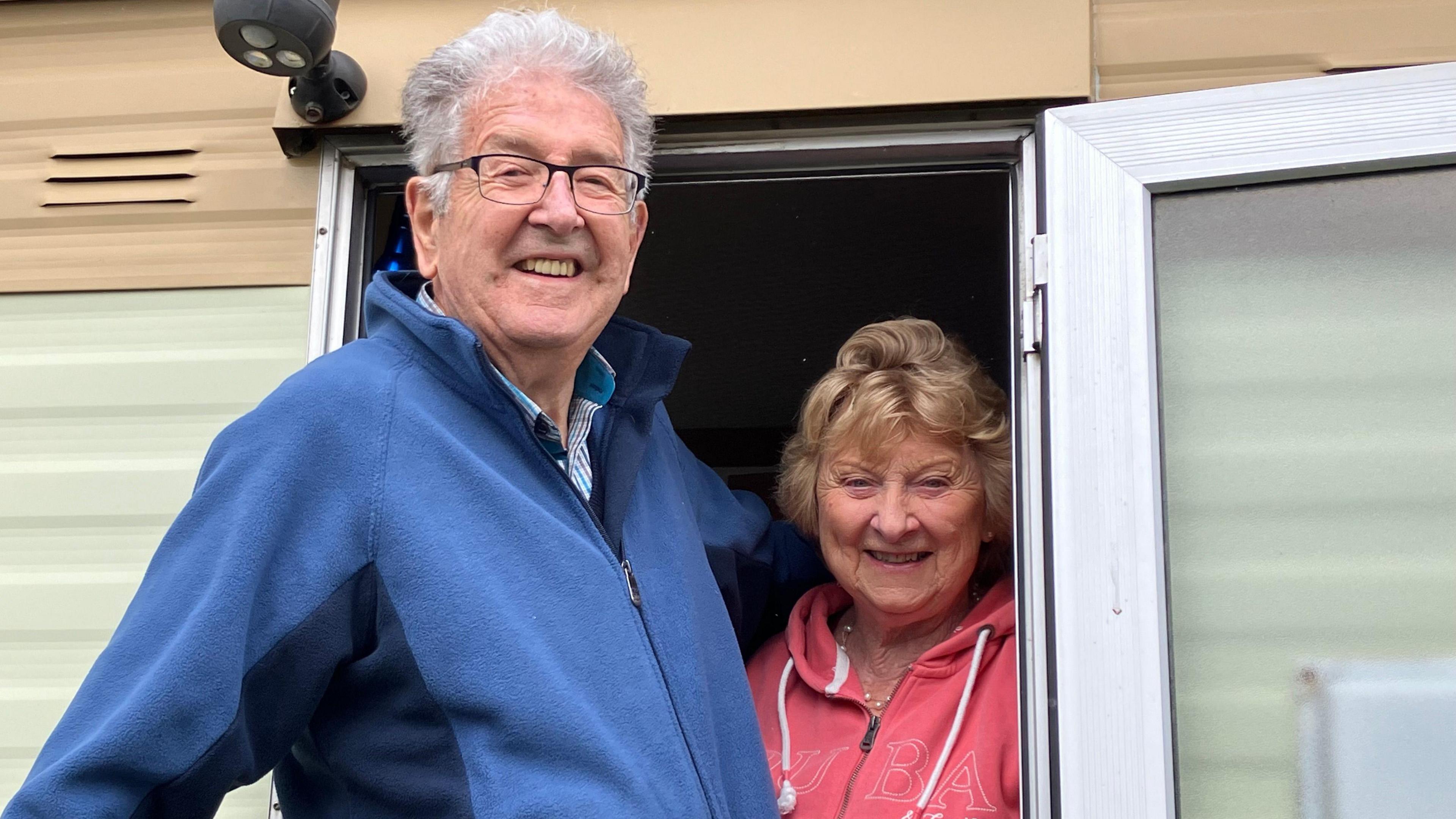 Cynthia and Bill Smith smile as they stand in the doorway of their caravan