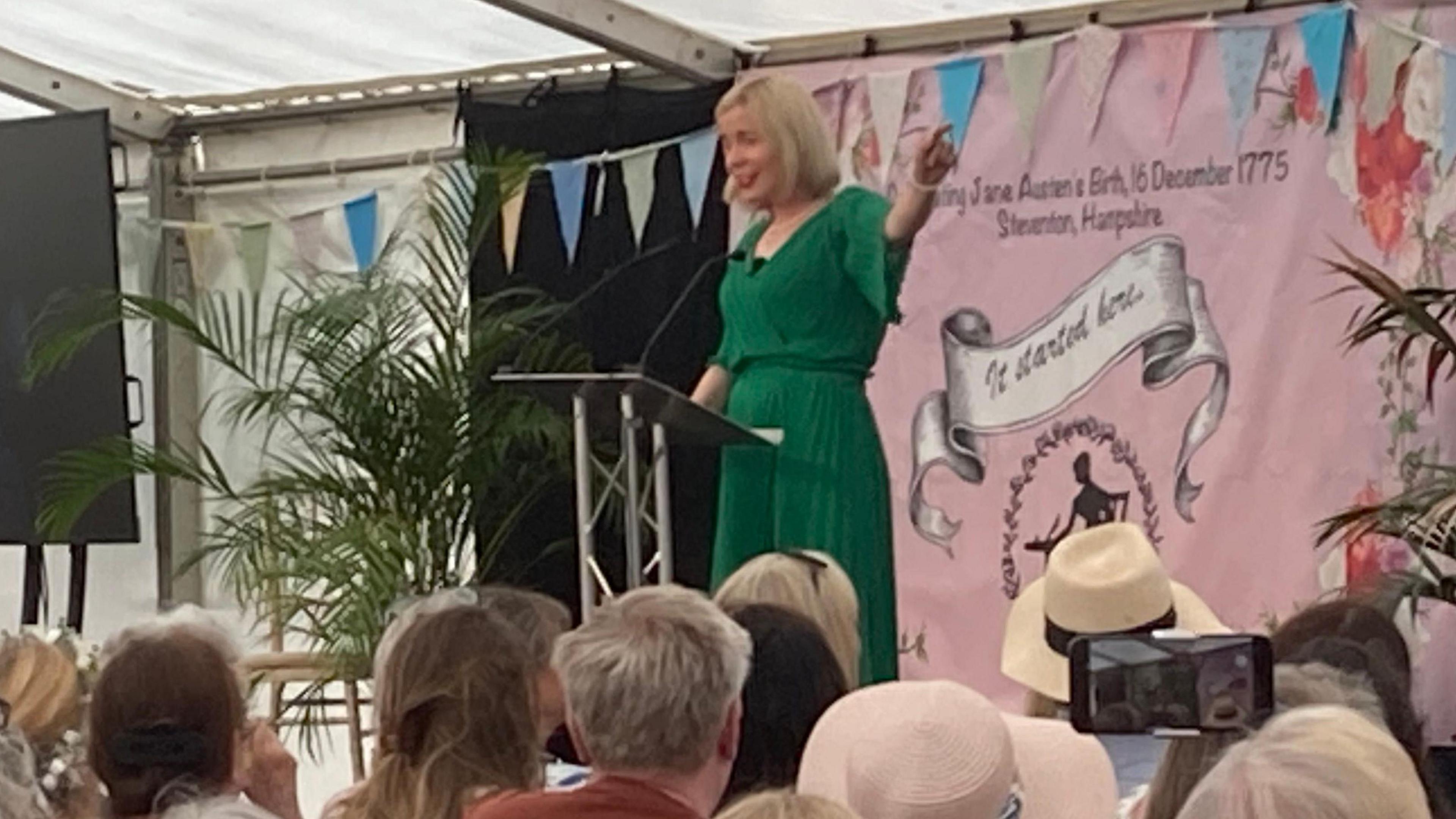 Historian Lucy Worsley in a green dress on a stage with an audience looking on as she gives a talk. 