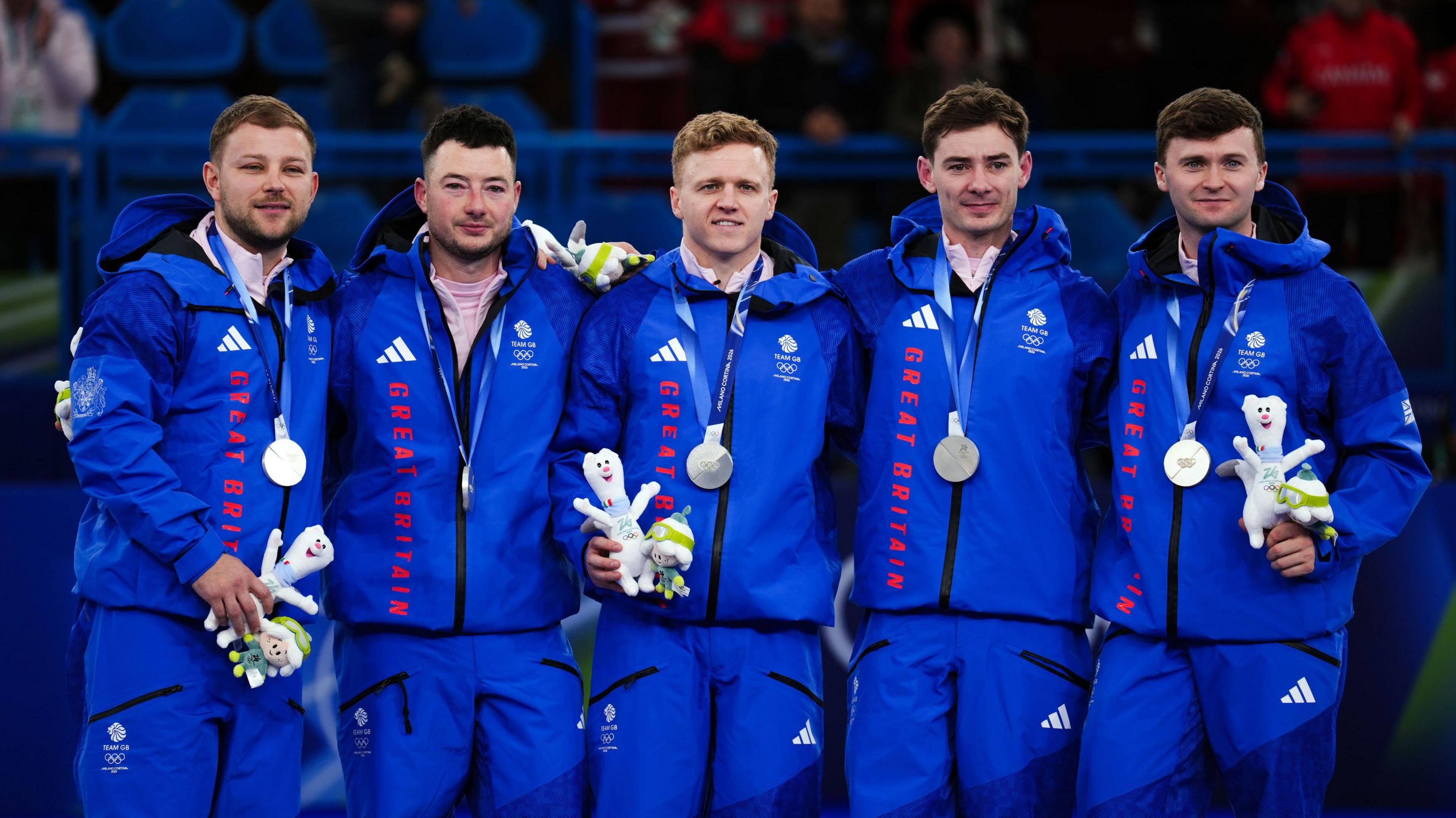 From left, Kyle Waddell, Hammy McMillan, Bobby Lammie, Grant Hardie and Bruce Mouat standing on the podium with their silver medals. They are all wearing blue Great Britain tracksuits.