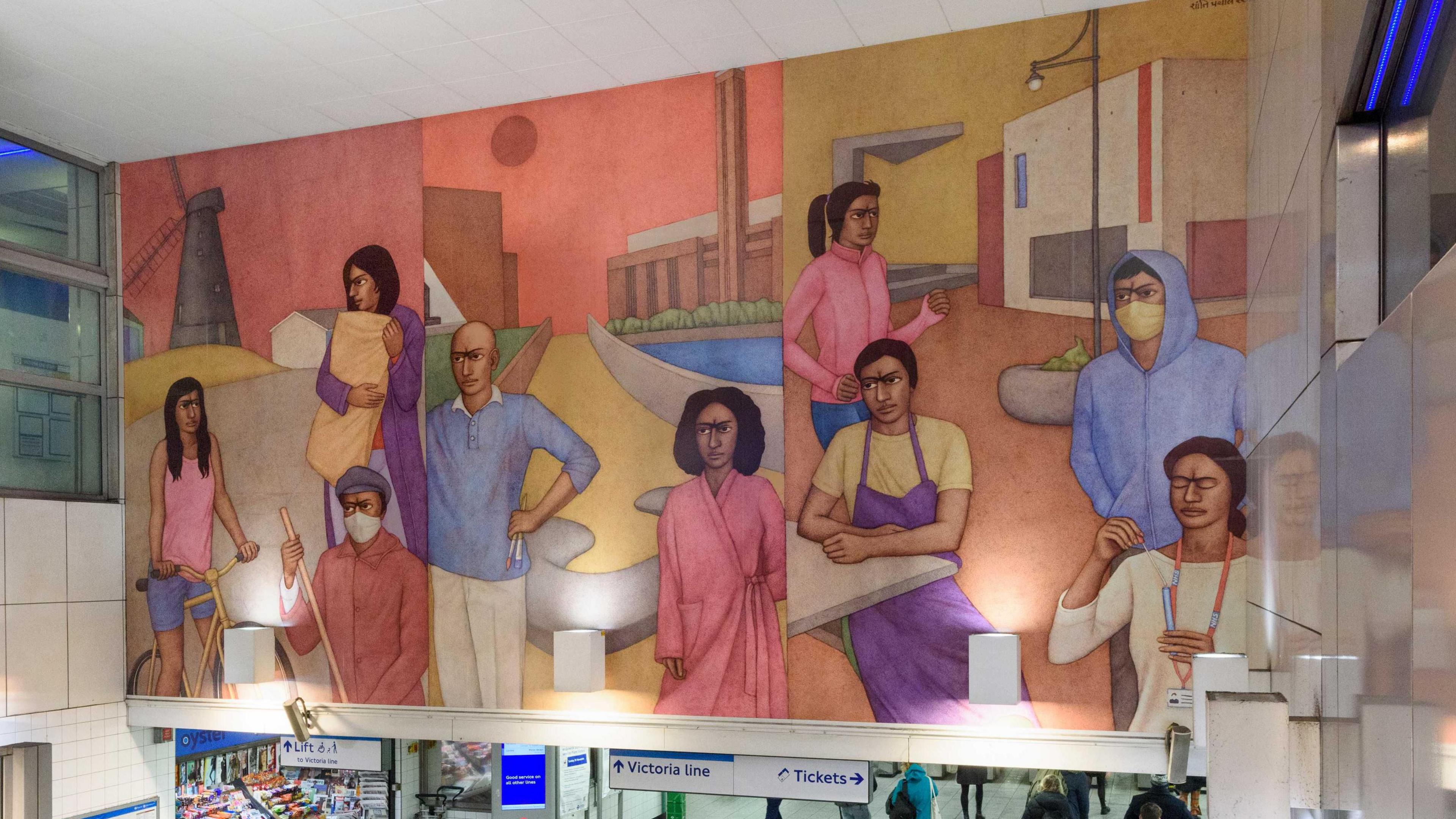 A large mural is installed over the entrance to Brixton Tube station. It features figures in three panels, in various poses including on a bike; some are wearing face masks. There is a windmill in the background of one panel.   