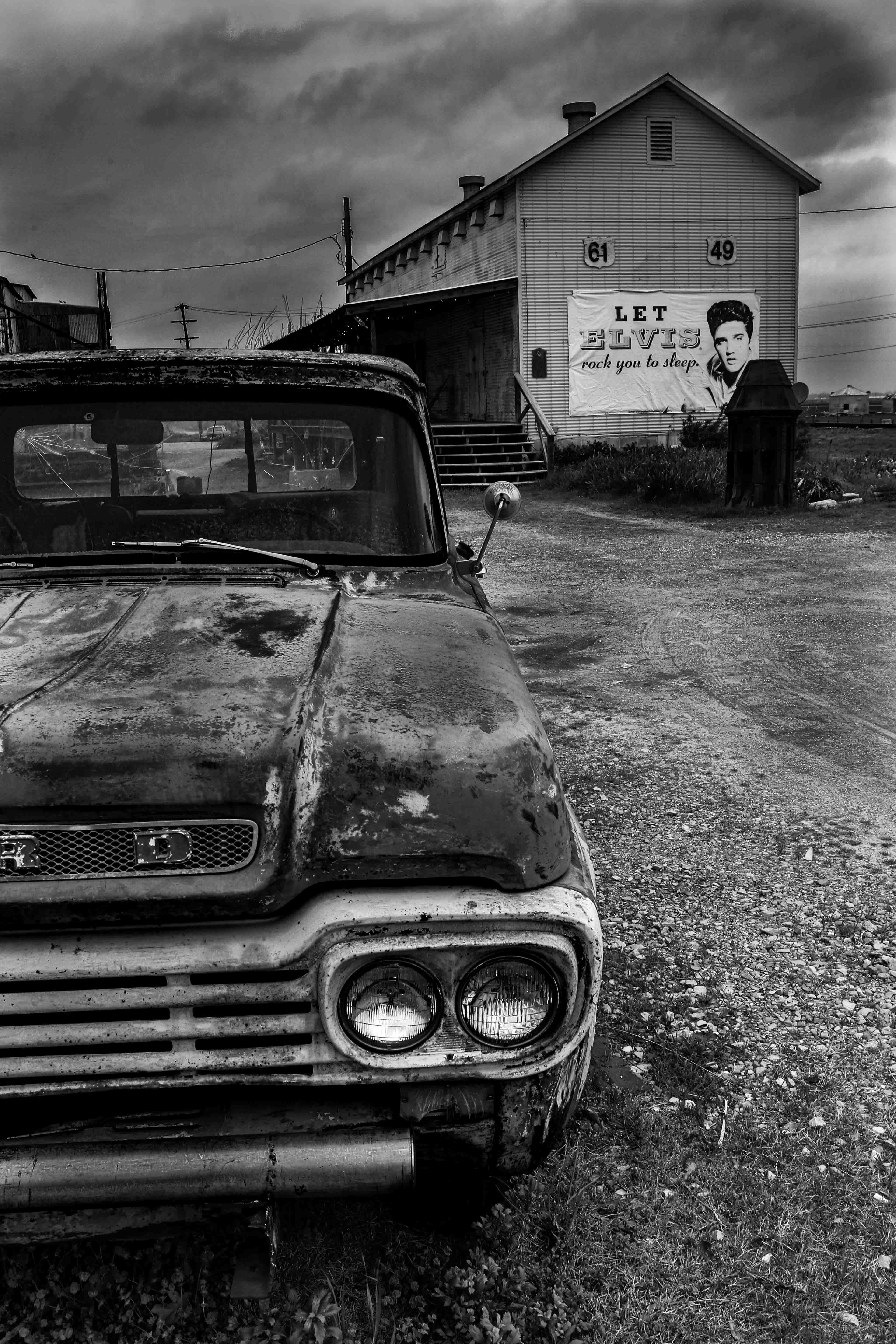 An old car is parked in front of a sign with a picture of Elvis