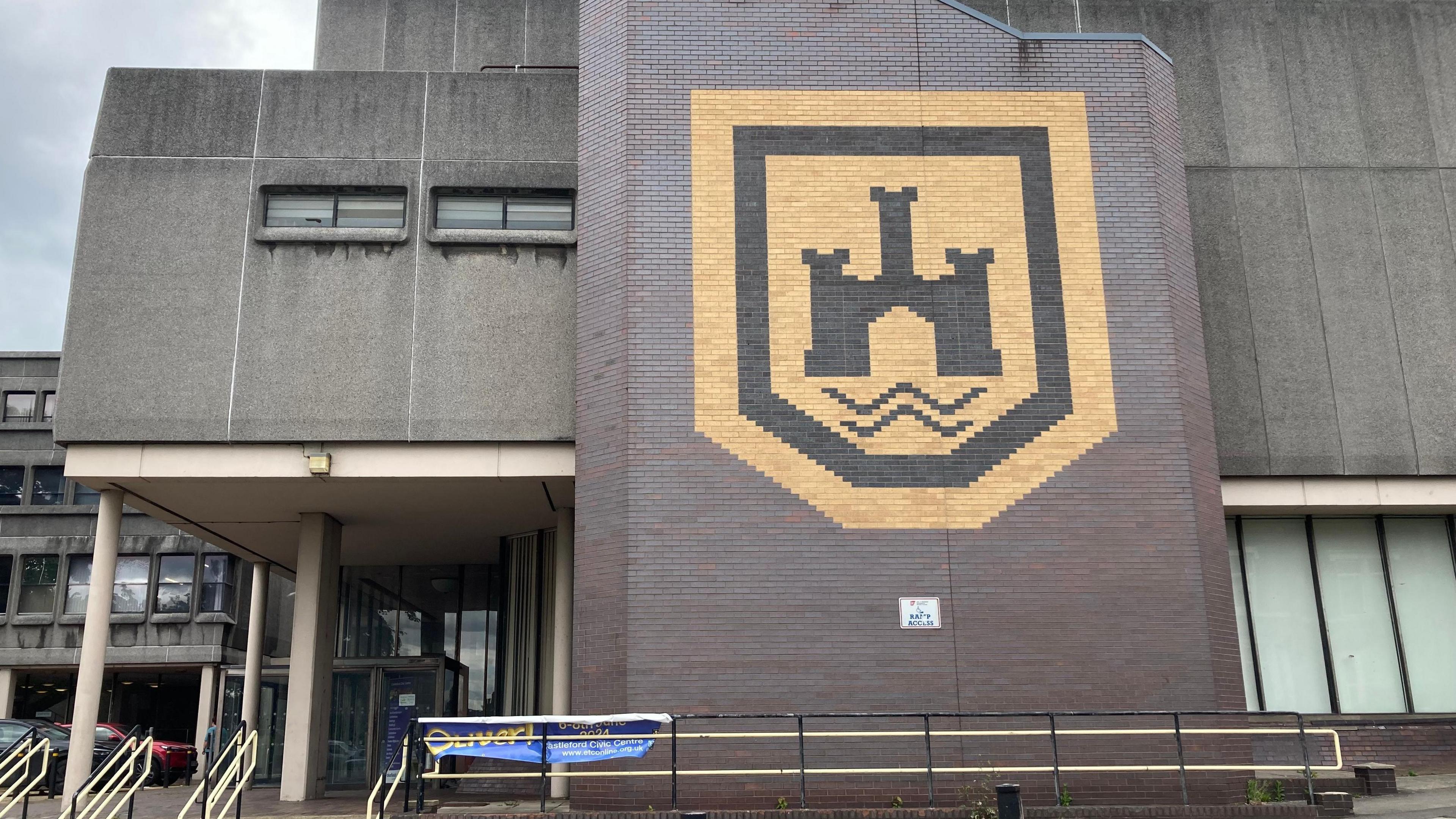 A grey brutalist 1960s building with a large yellow and black logo on the front.