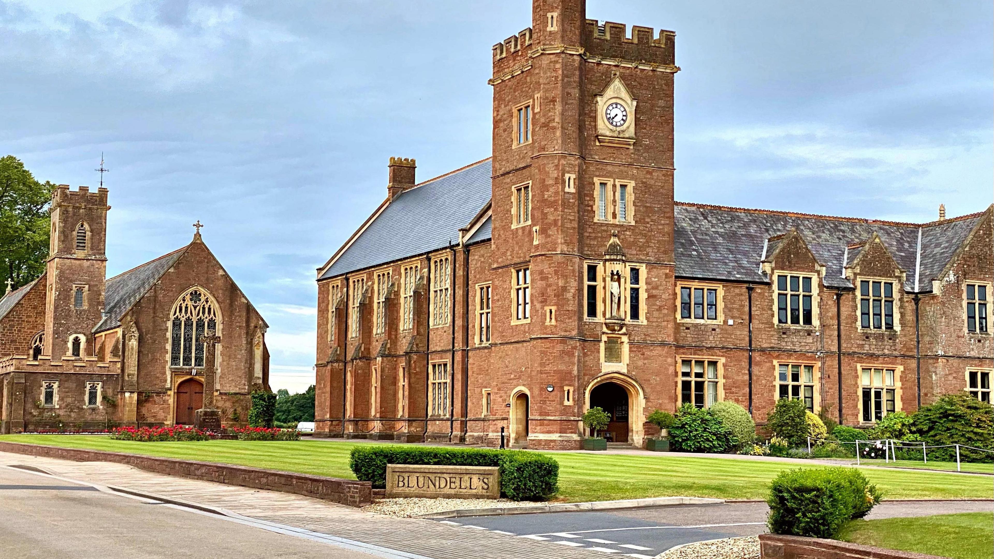 Entrance to Blundell's School, Tiverton, Devon. A green lawn is pictured in front of the large brick building. 