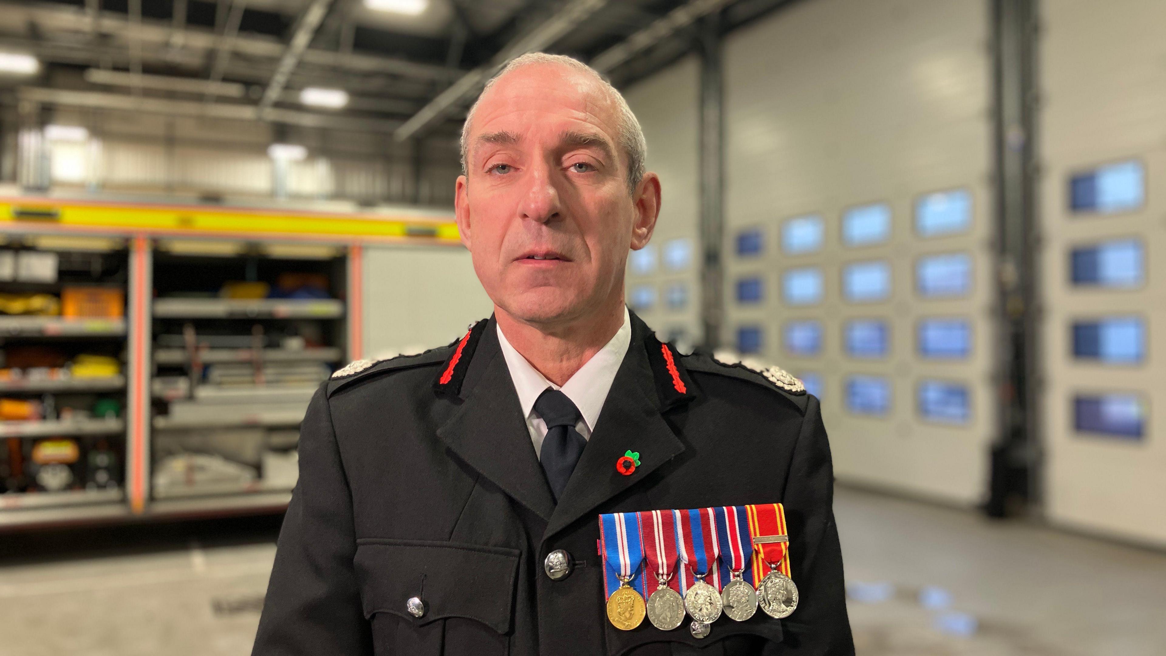 Simon Shilton, pictured inside a fire station. He is looking directly at the camera and is in uniform, with five medals and a small poppy badge attached to his blazer. 