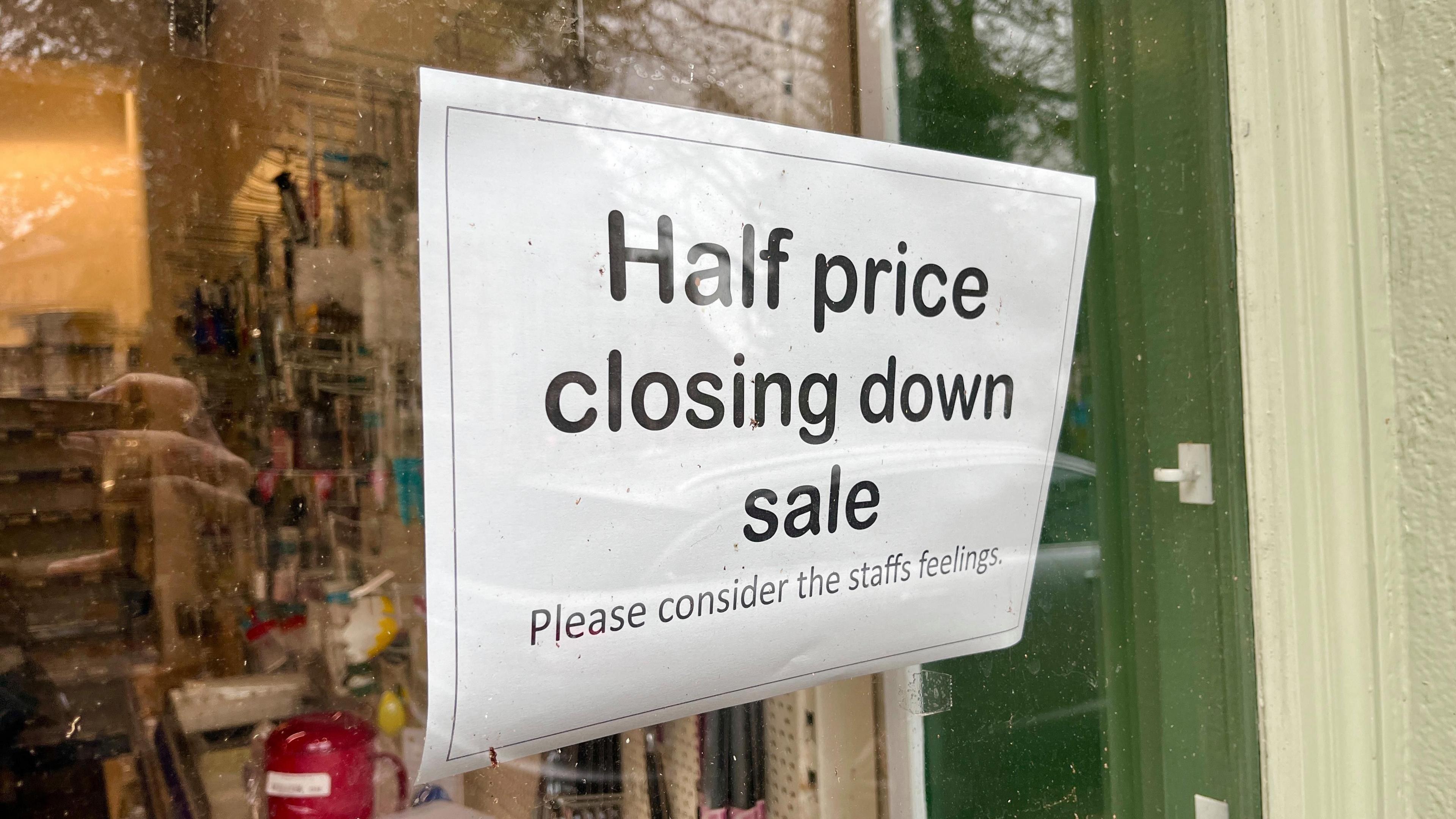 A sign saying 'half price closing down sale - please consider staffs [sic] feelings' stuck in the window of the shop