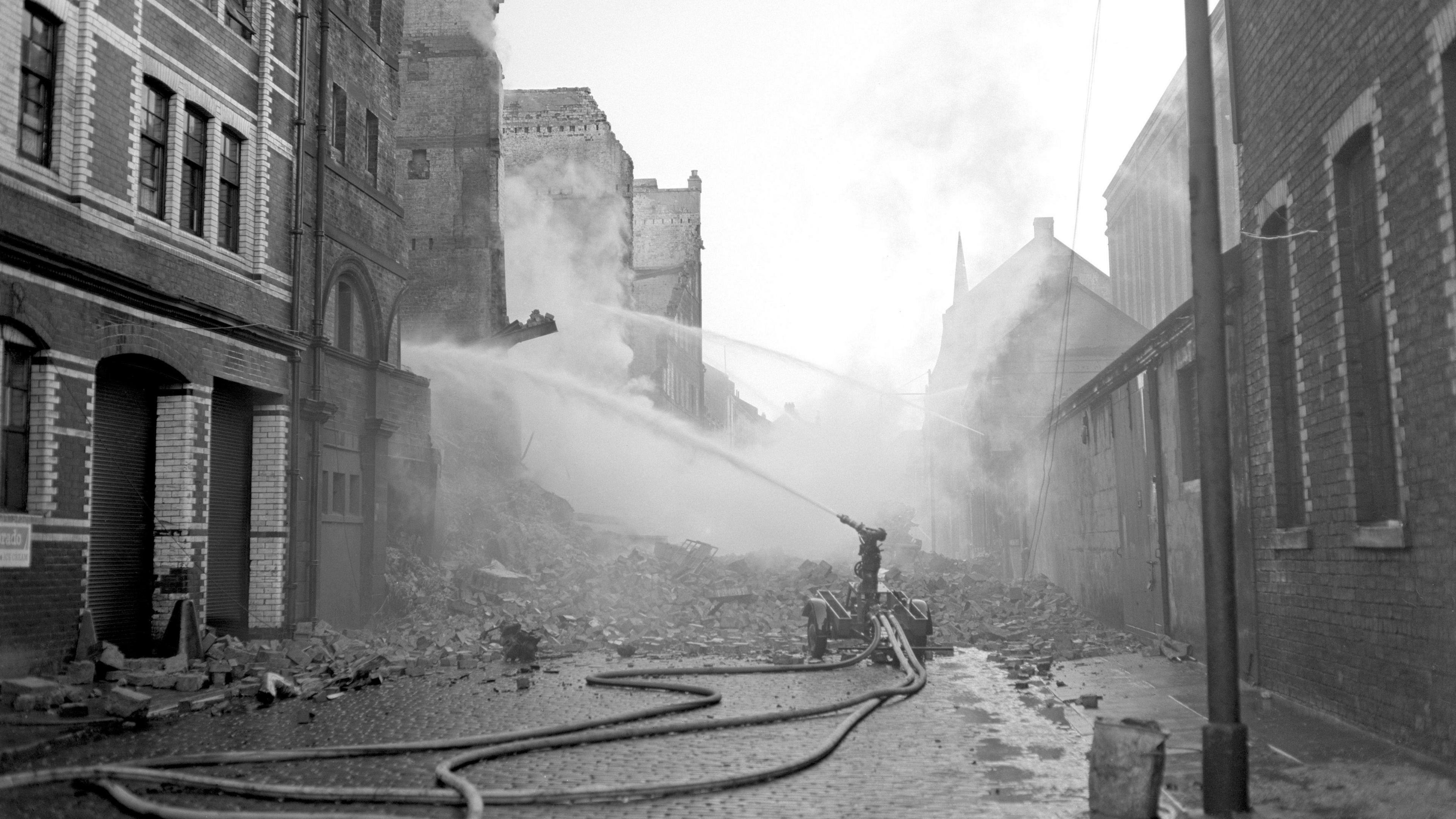 A black and white photograph of hoses being fired at a building at Cheapside Street following the fire in 1960.