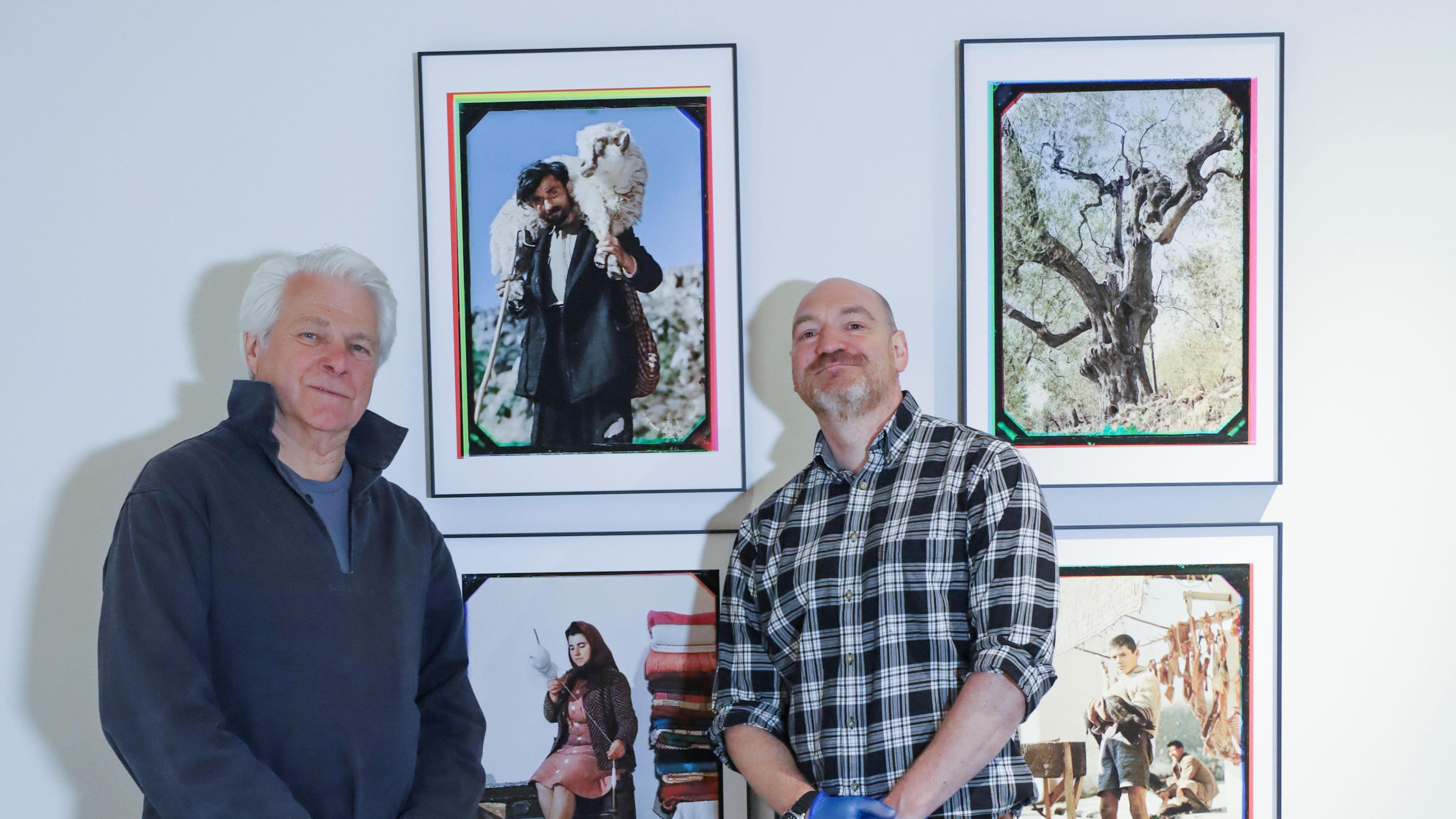Two men, one in plaid, the other in a pullover, looking at the camera with a selection of four photos in the background. The photos are of a shepherd carrying a sheep, a tree, a woman sitting down and a boy standing up.