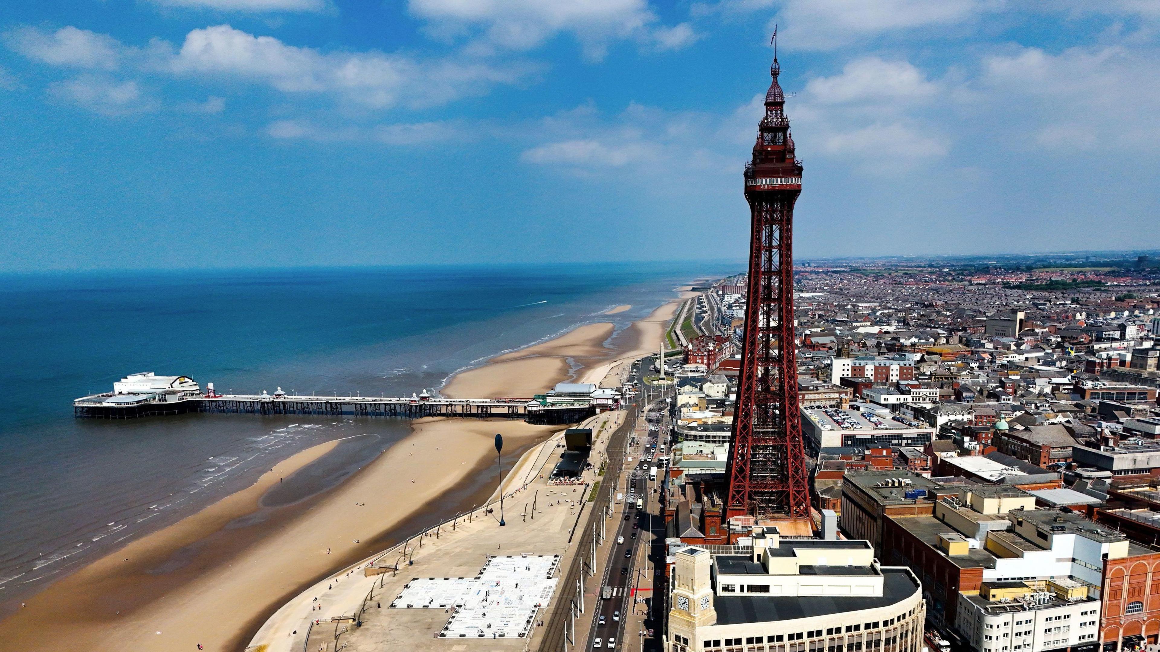 Blackpool Tower in the heart of the town with a jetty to the left over the sandy beach and houses and other buildings to the right