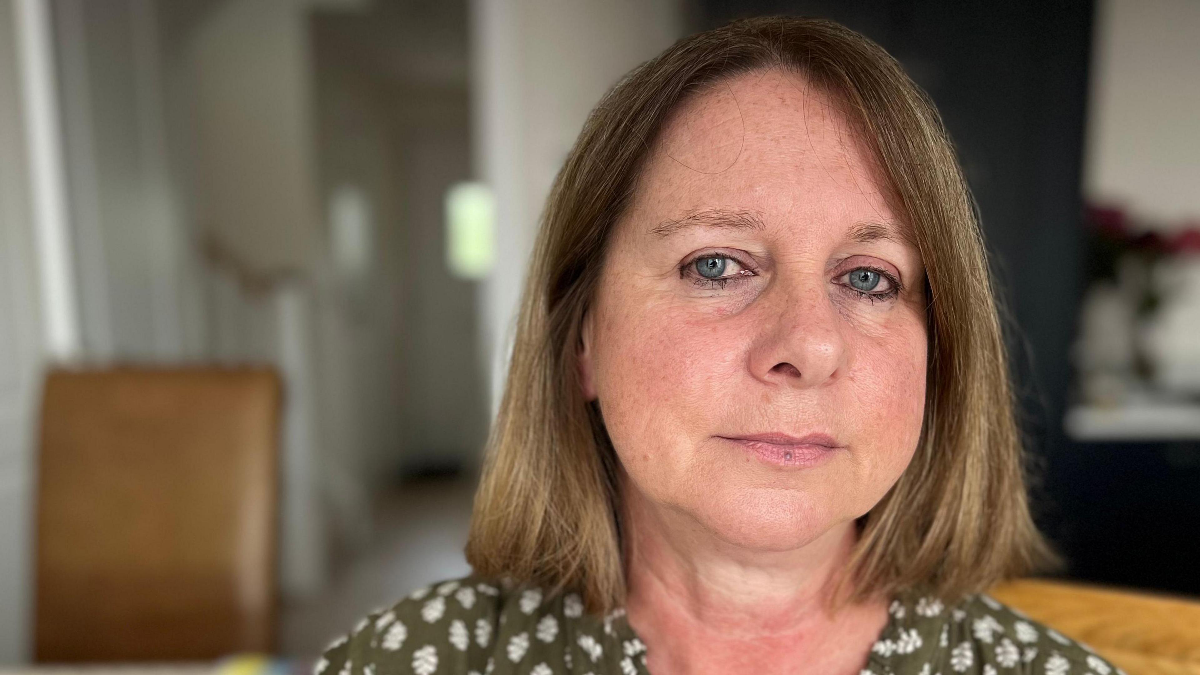 A white woman with brown / blonde hair is sitting looking directly at the camera. 