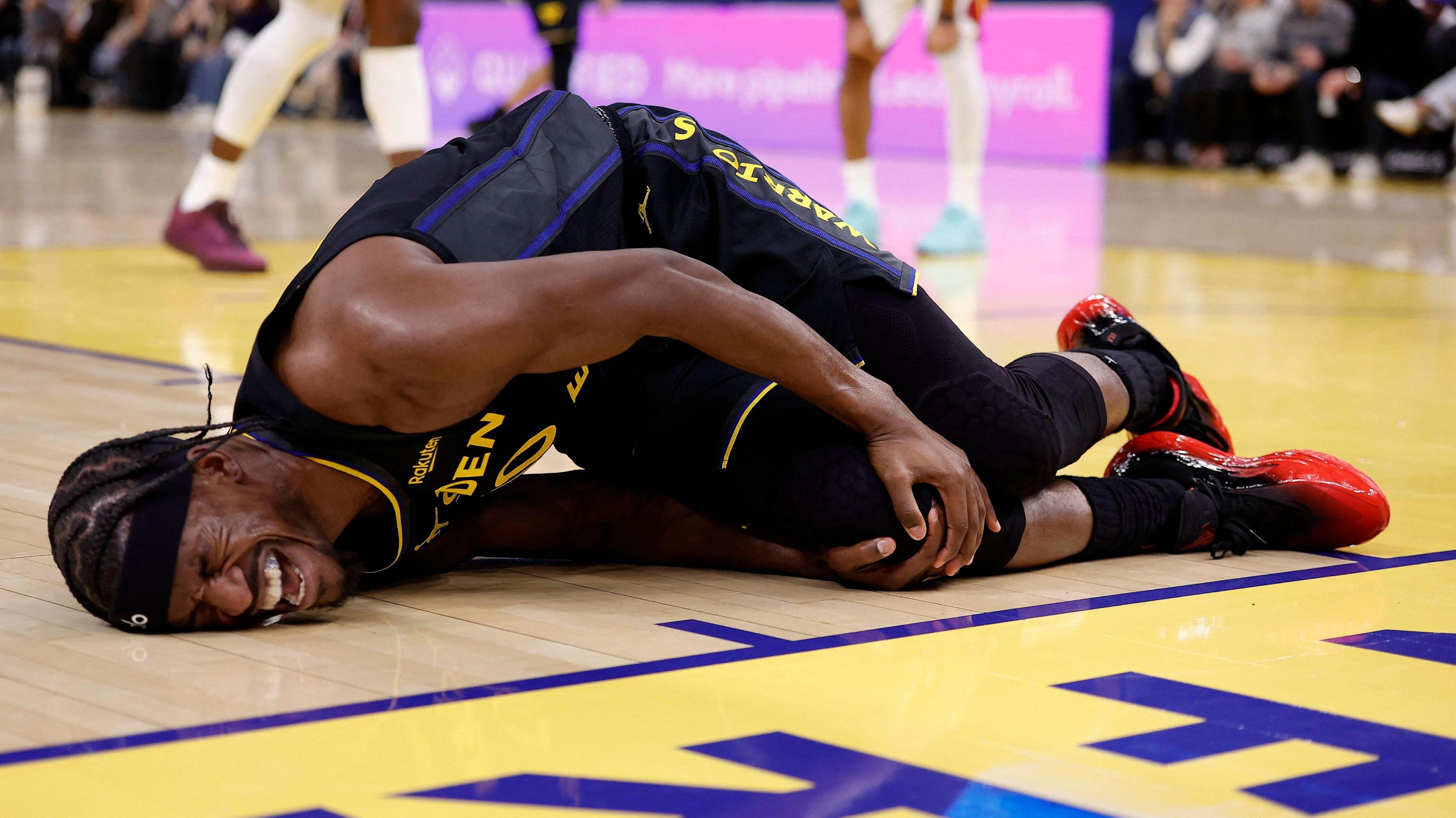 Golden State Warriors forward Jimmy Butler lies on the floor in agony, holding his right knee after tearing his ACL