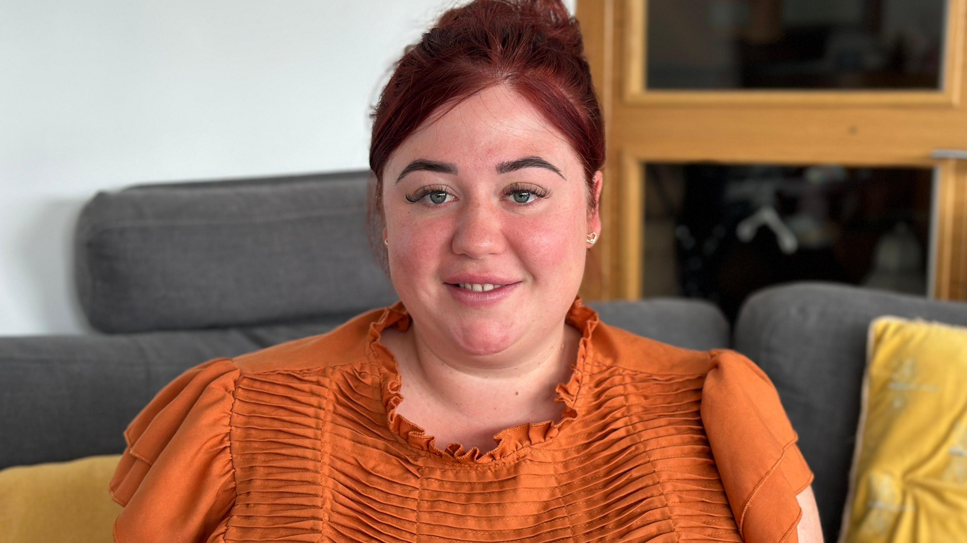 Naomi Allsop sat on a sofa wearing an orange top