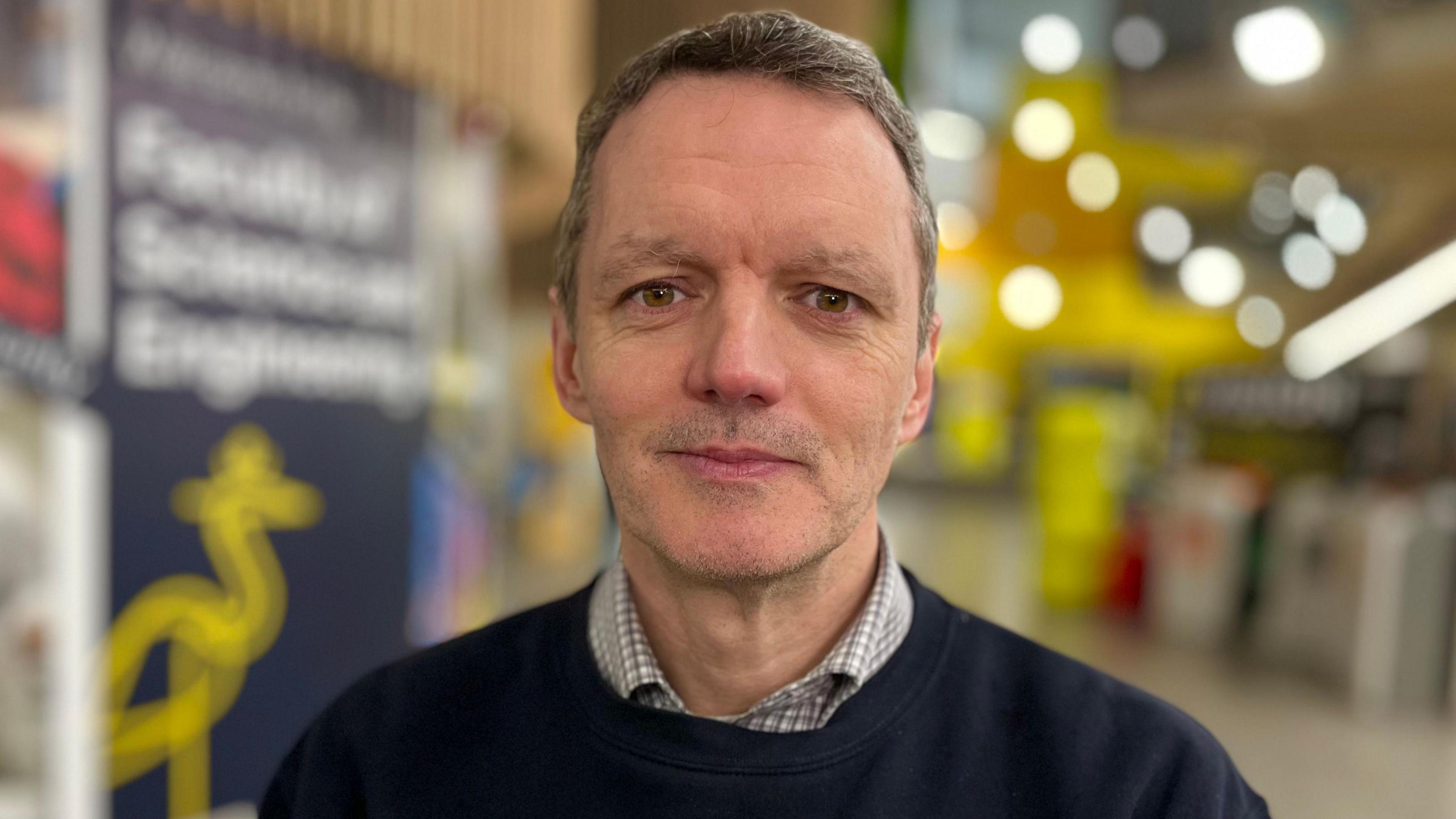 Aled Jones, in the background is a blue and yellow banner for the Faculty of Science and Engineering with ARU's crest on it