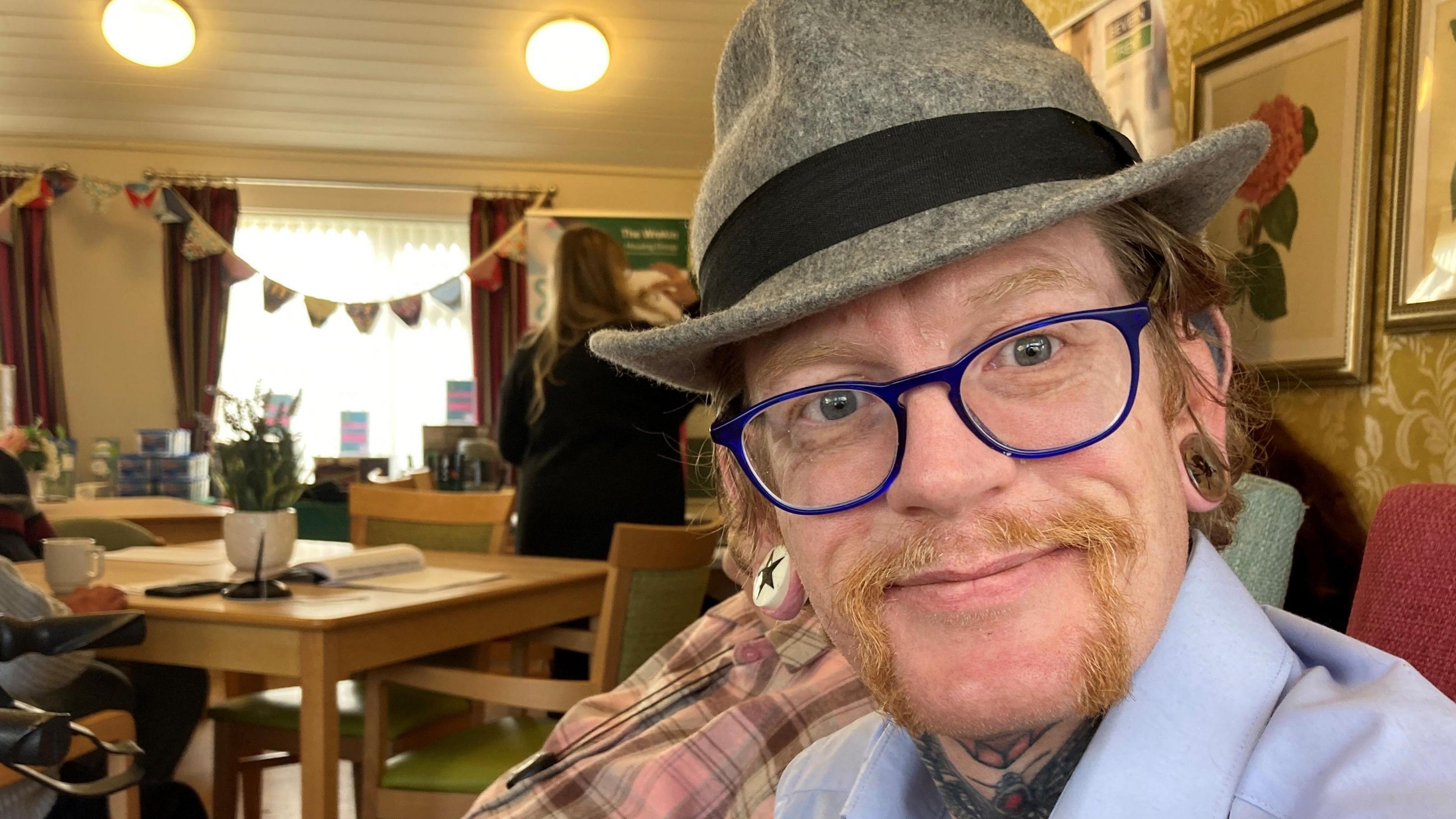 A middle-aged man wearing glasses and a hat is sitting with other people in a lounge at the Stallard Court retirement complex in Oakengates.   