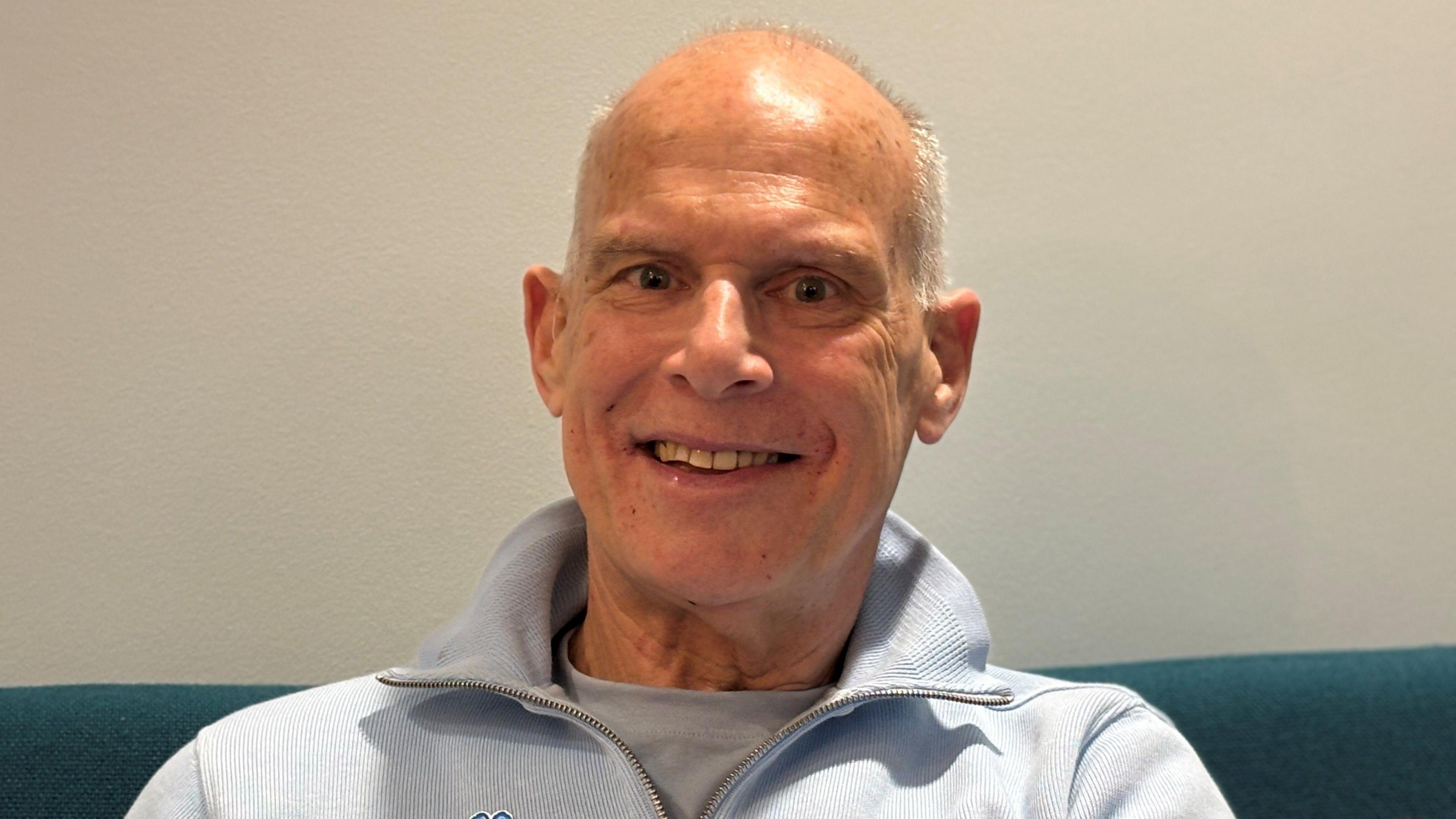 Smiling Alan, wears the blue flower badge of Alzheimer's Society charity