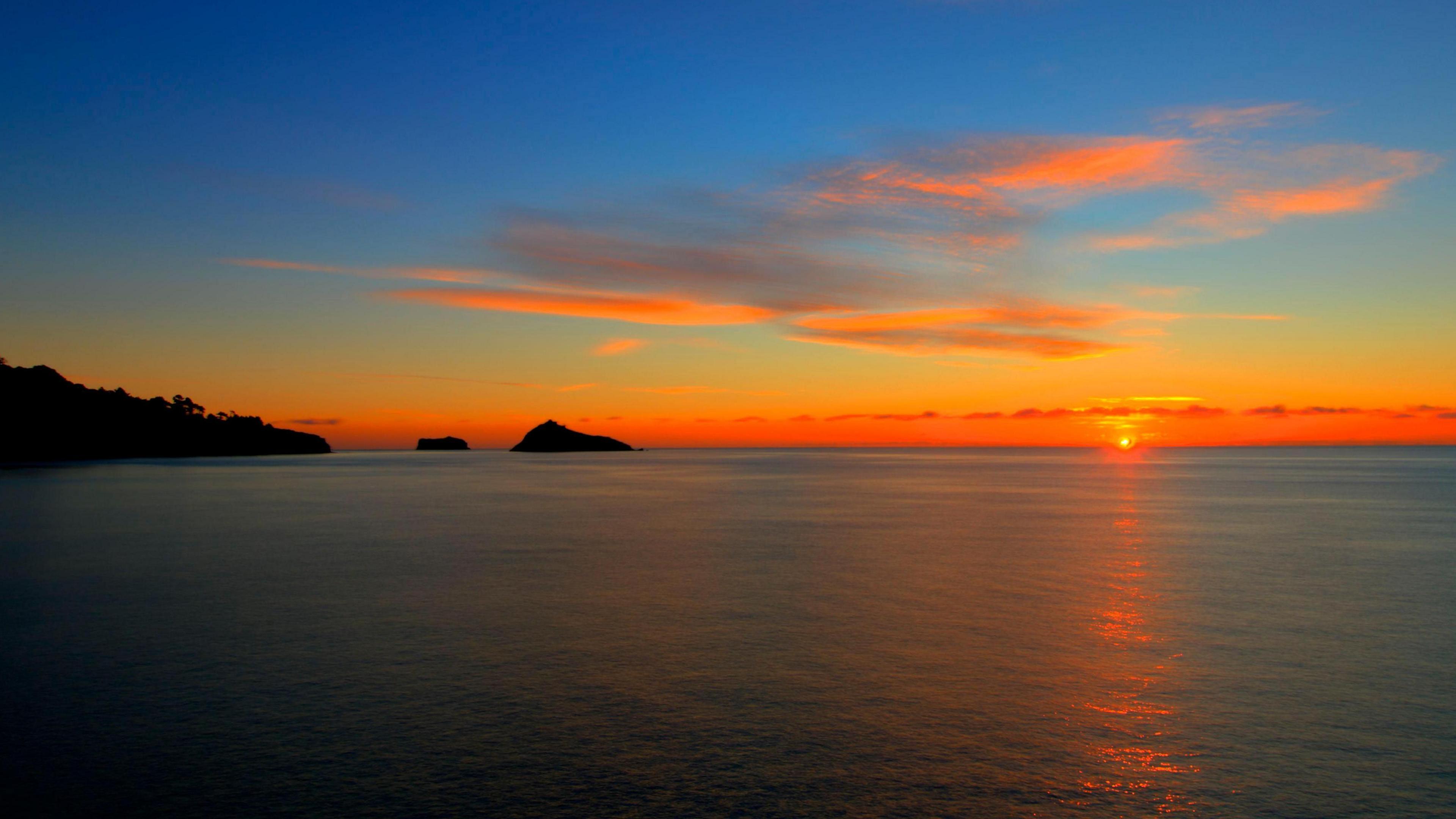 The sun rises over the coast near Torquay. It has given the sky a tinge of orange. Light cloud cover is in the sky.