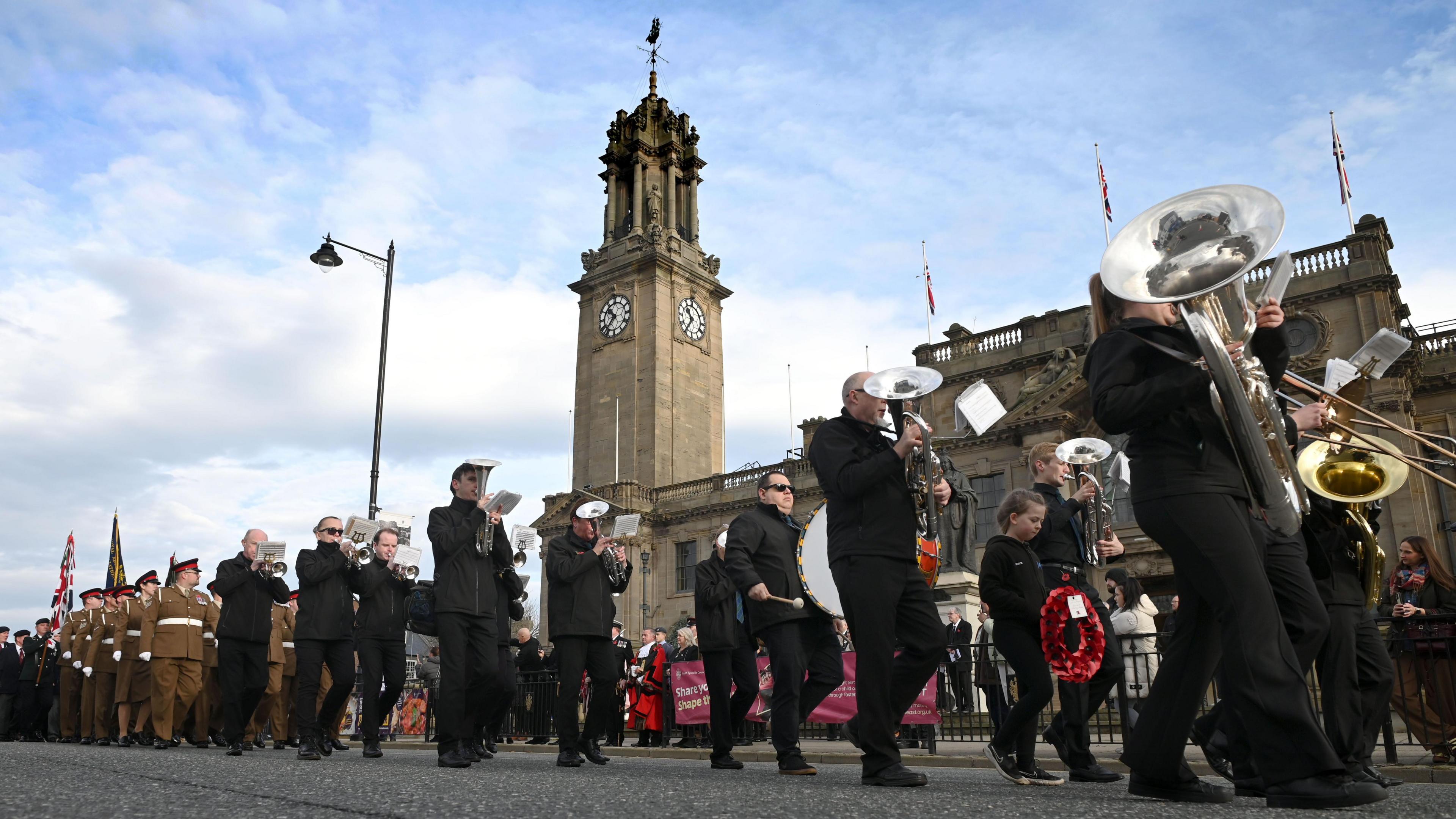 A parade made up of servicemen and women and musicians playing brass instruments marches through Westoe in South Tyneside.