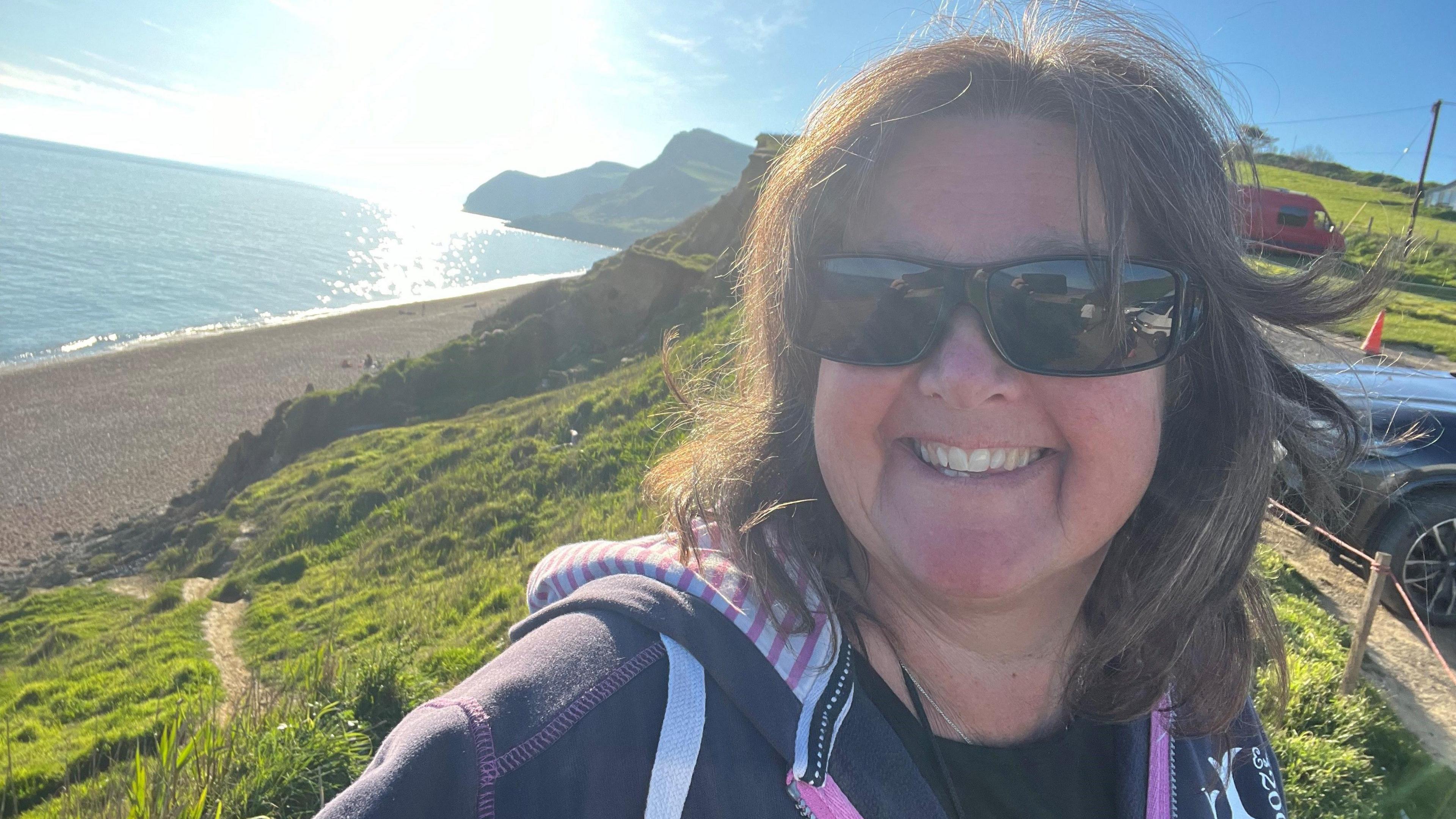 A selfie of Angela smiling from a cliff overlooking the sea