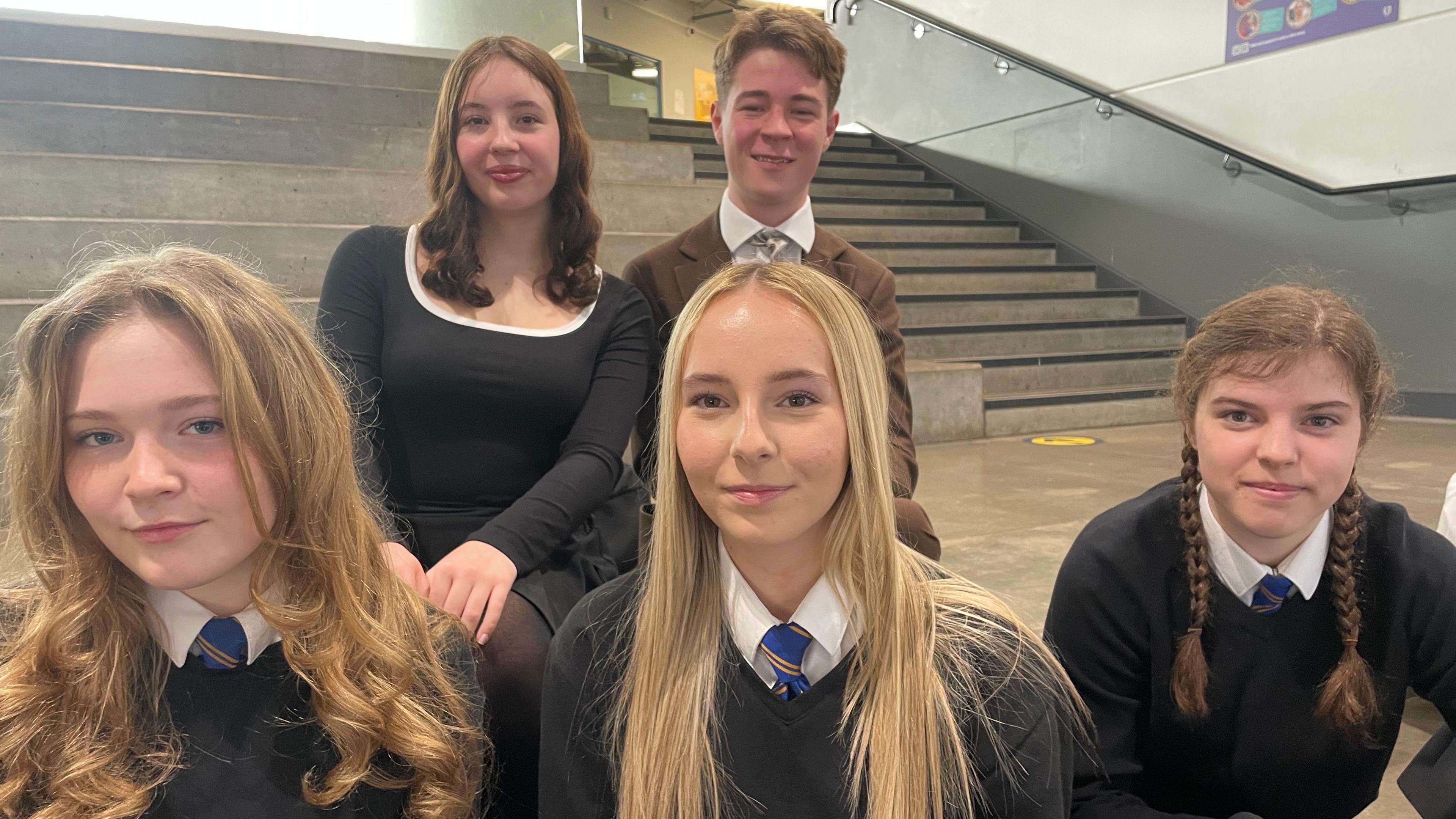 Five pupils - four girls and two boys sitting on steps in a school