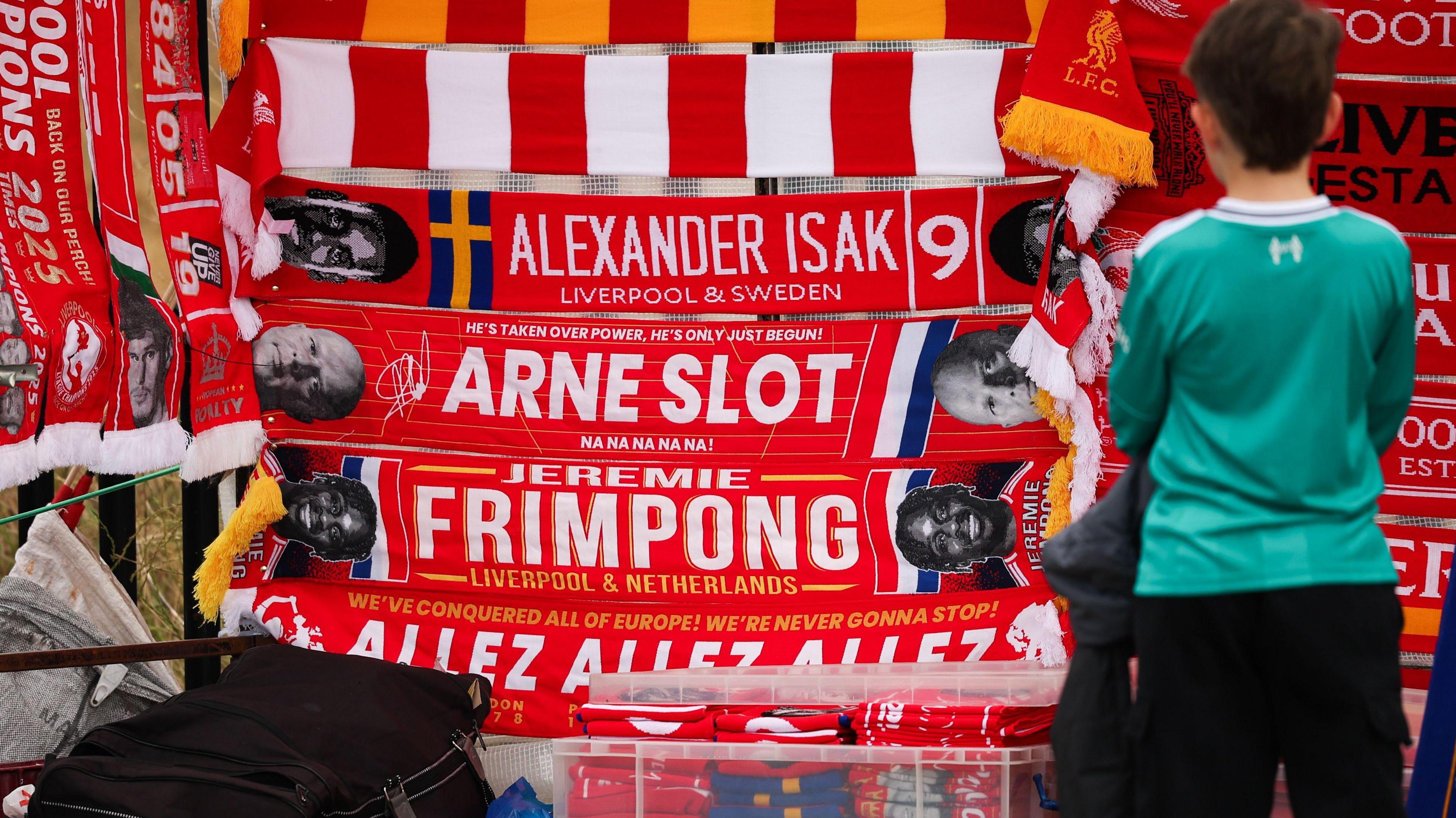 A wide shot of a child looking on at a selection of Liverpool scarves.