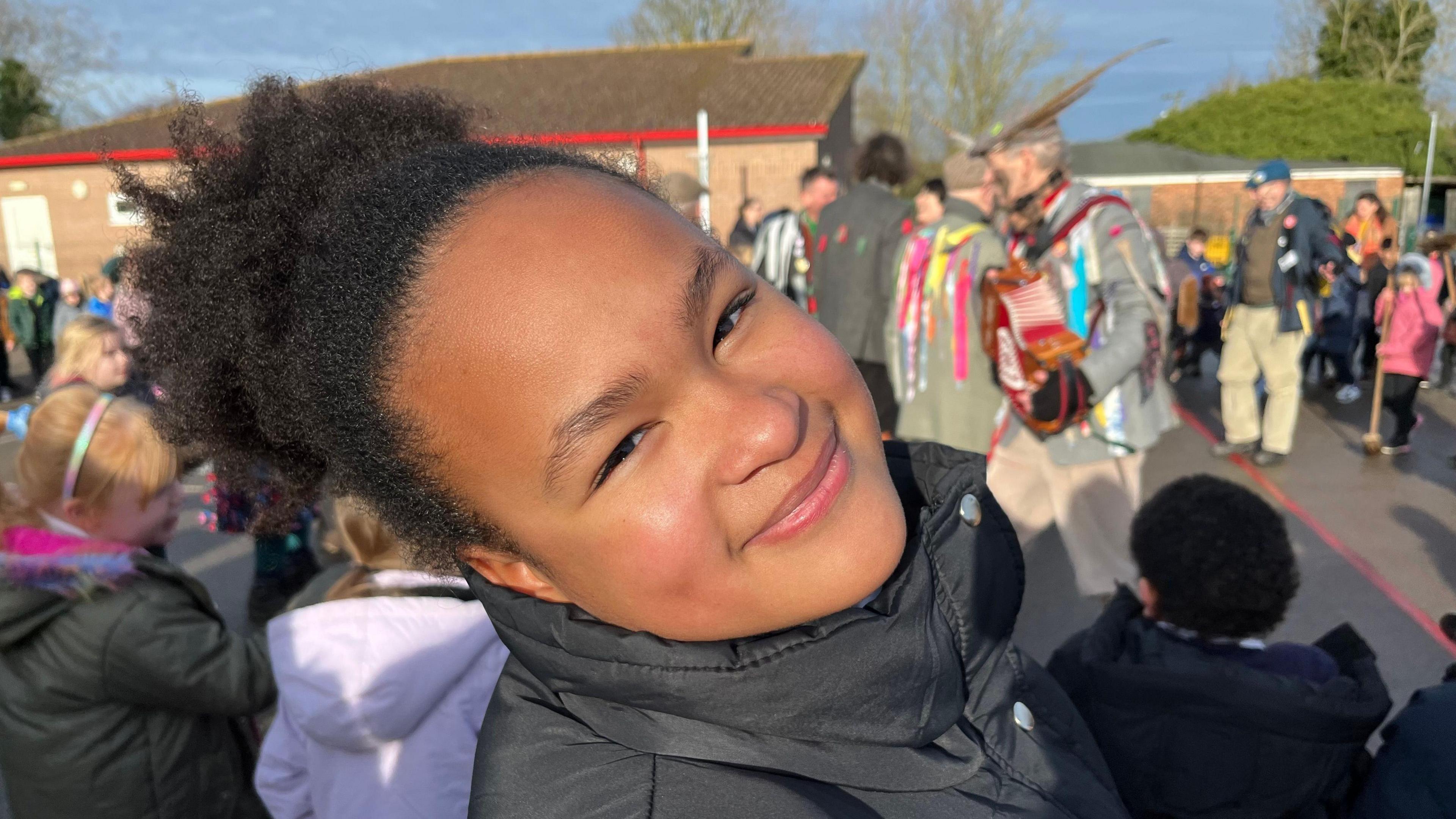 Victoria,10, has a black high collared coat on she is smiling and has her head tilted back. She has black hair tied up above her head.