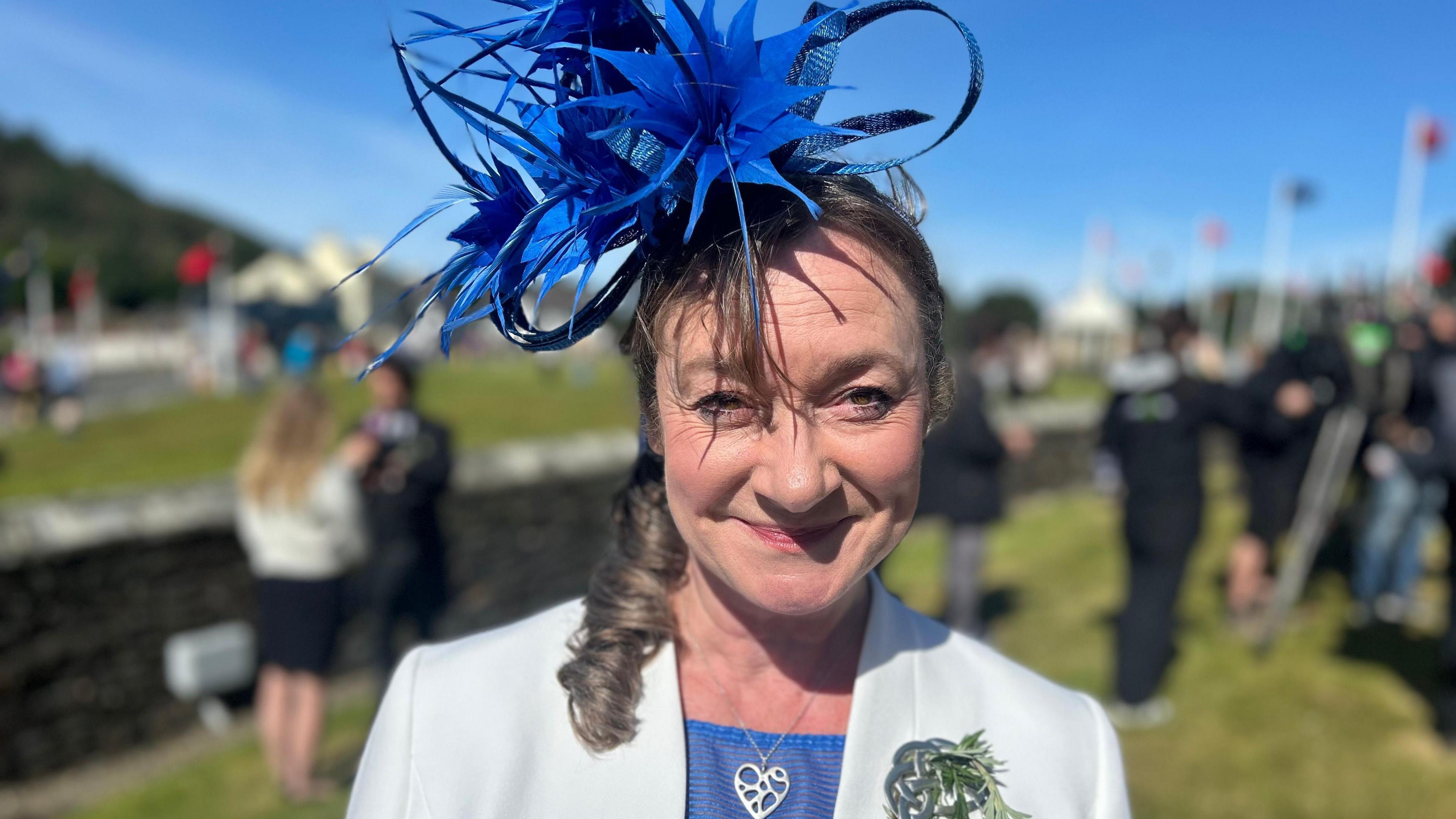 A woman smiling with curly hair and an extravagant blue hat (Daphne Caine_