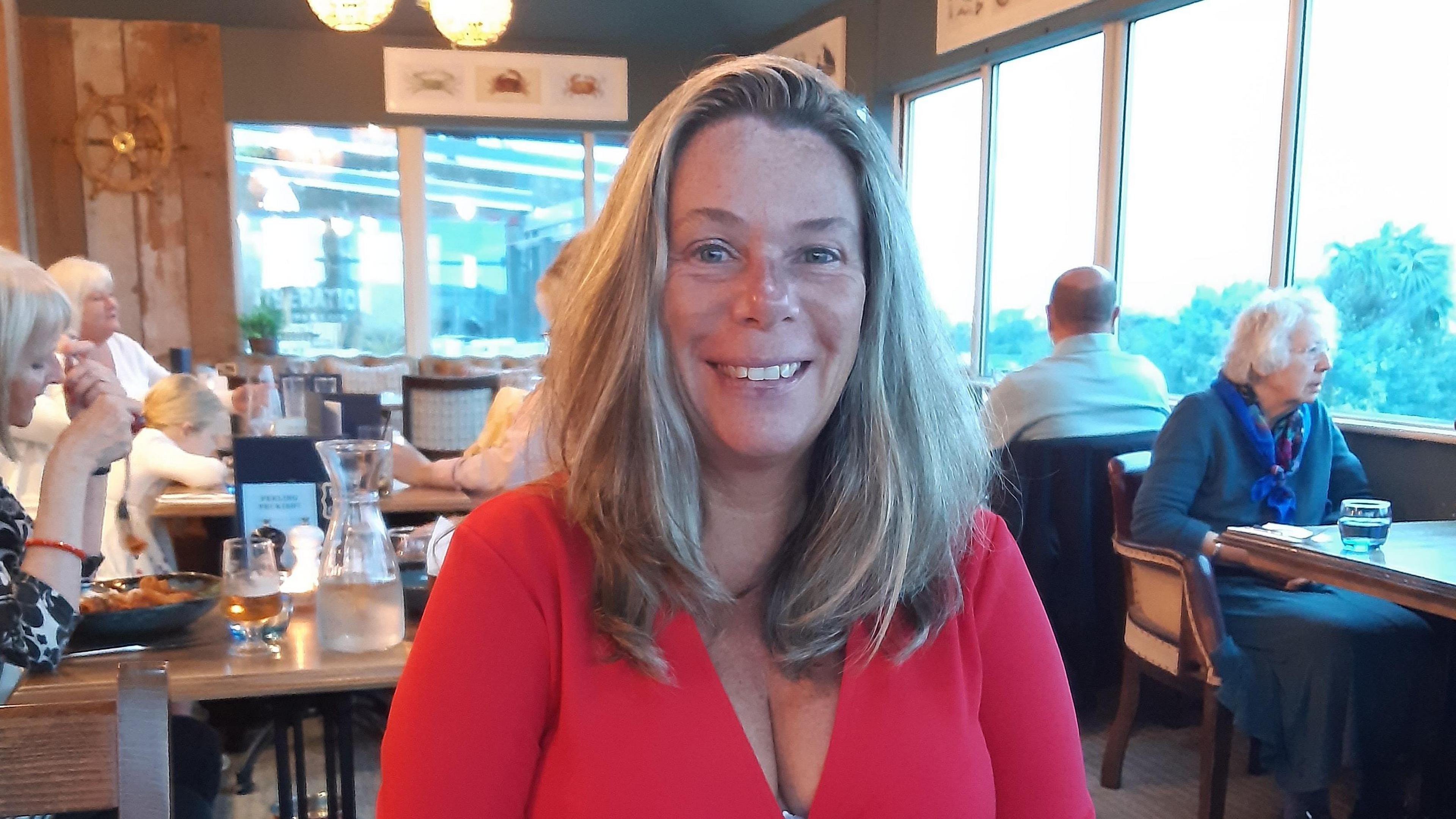 Jess Mauger smiles at the camera, she is wearing a red dress and has long fair hair.